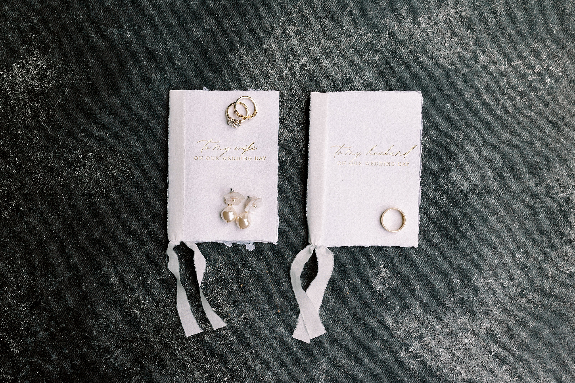 gold jewelry rests on ivory vow booklets with white ribbons