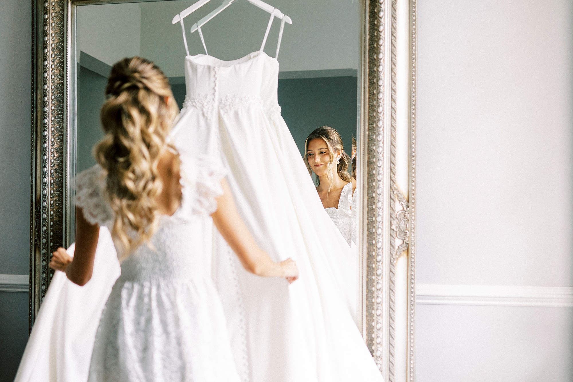 bride looks at wedding gown hanging on gold framed mirror at Separk Mansion