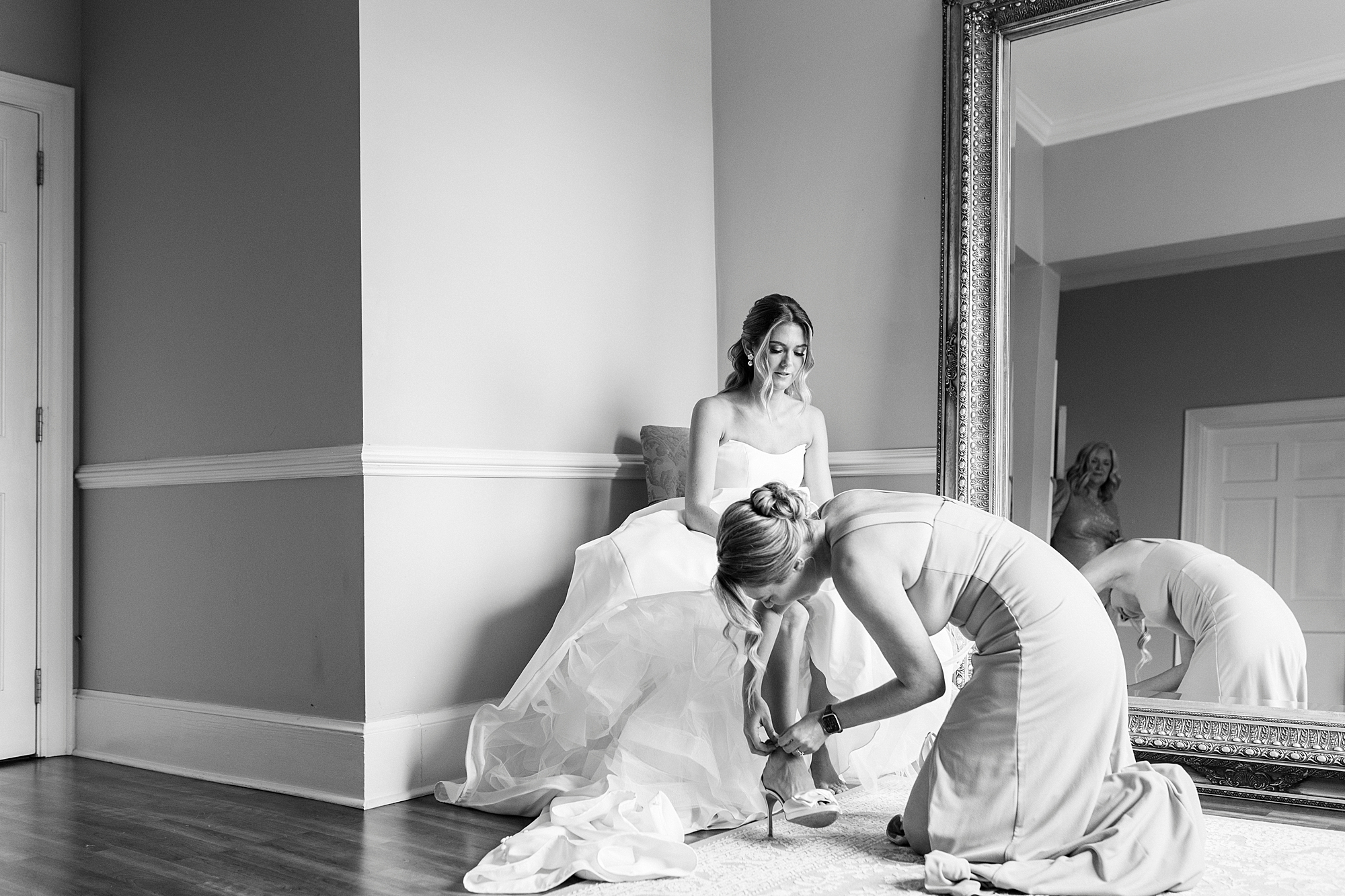 bridesmaid kneels to help bride into shoes for wedding day
