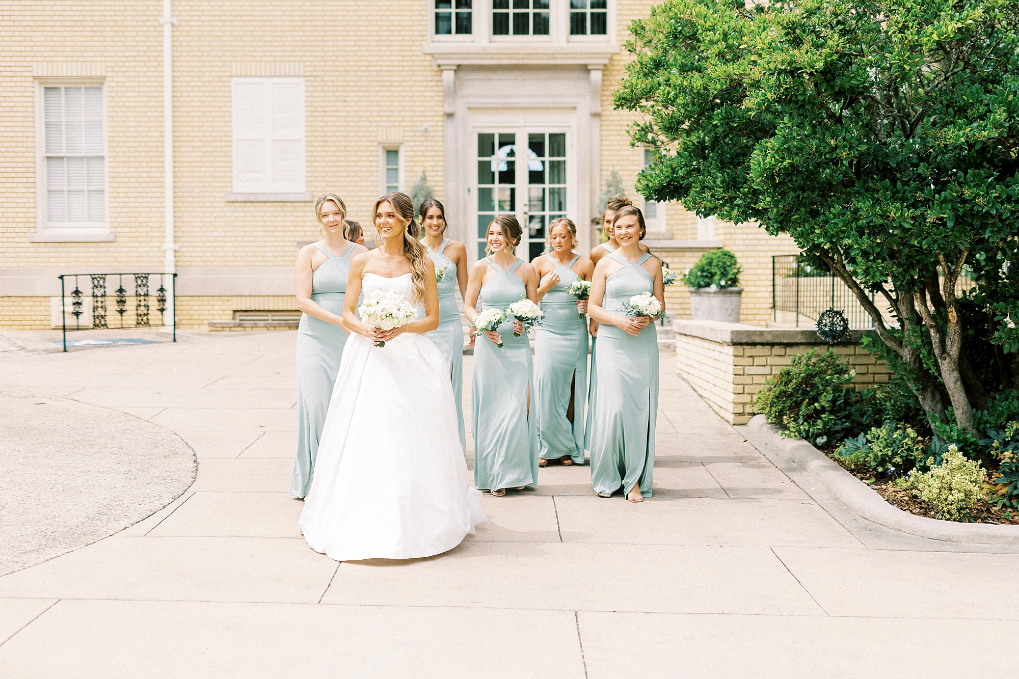 bride walks into garden with bridesmaids in blue gowns behind her