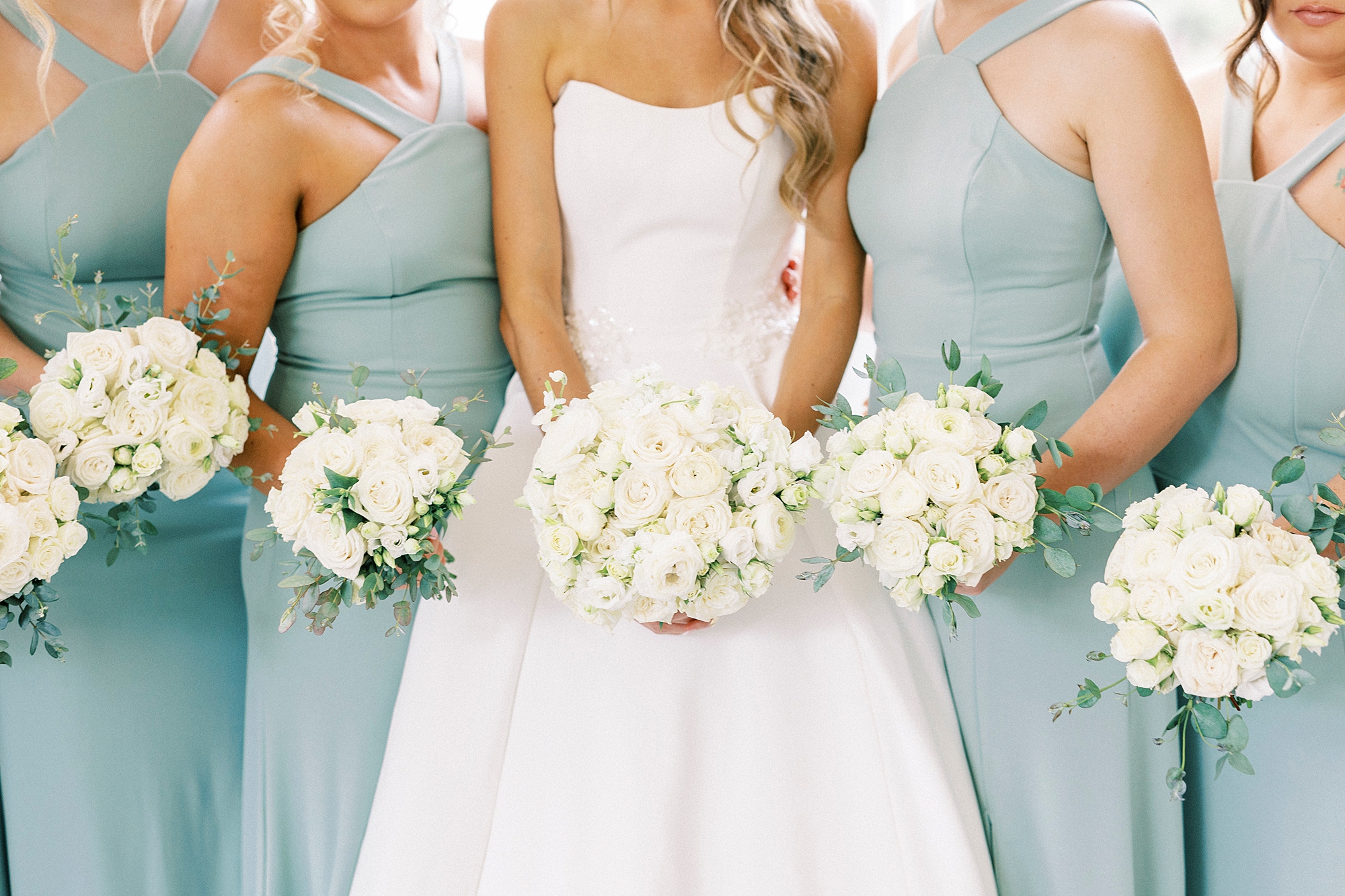 bridesmaids in light blue gowns hold white bouquets 