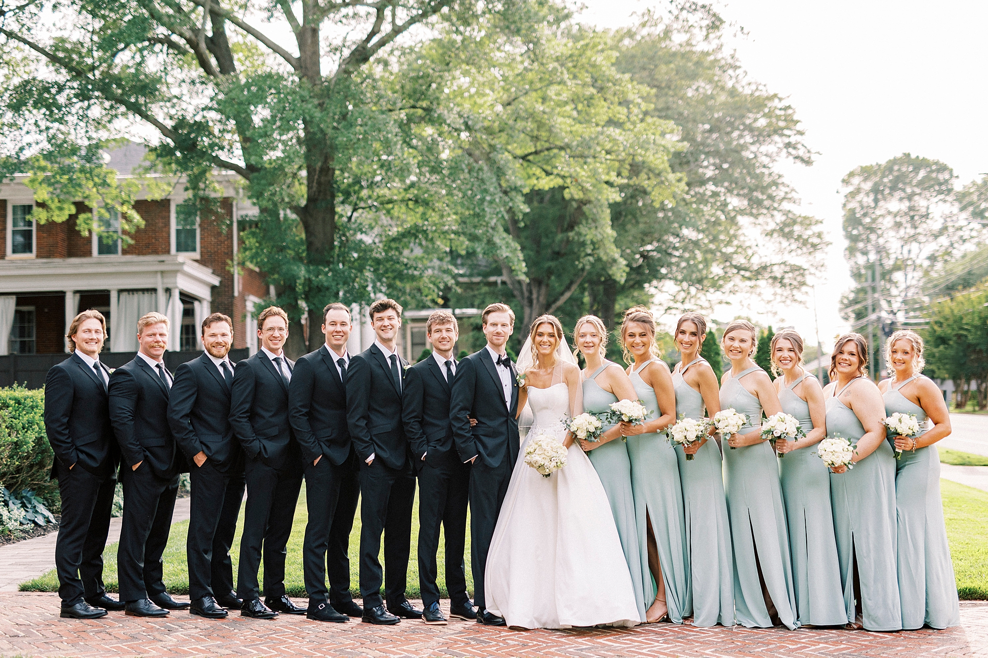 newlyweds pose with wedding party in blue dresses and black suits
