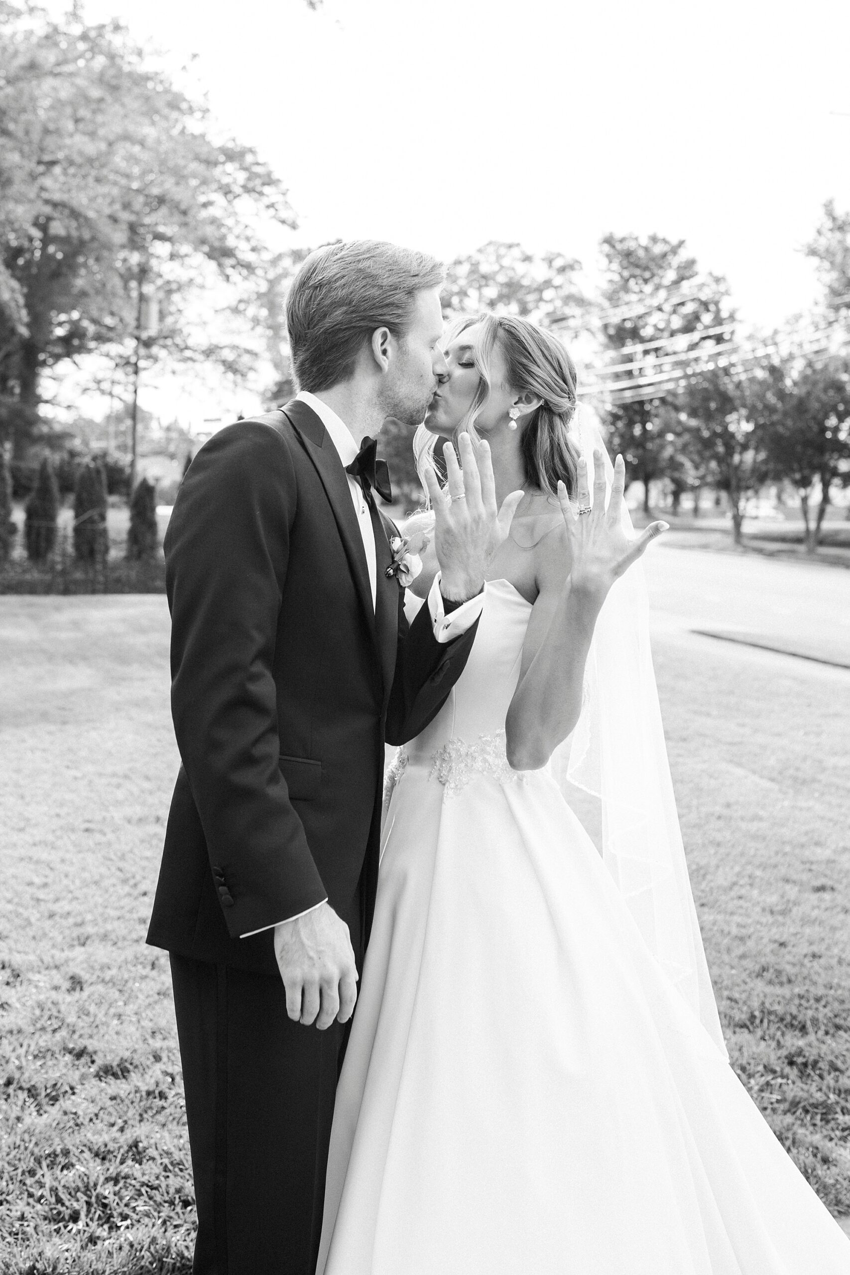 bride and groom kiss holding up left hands and showing off rings 