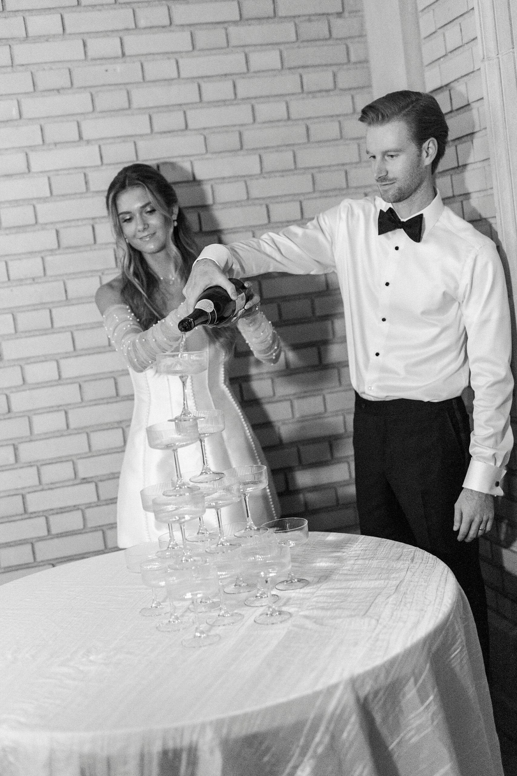 bride and groom pour champagne down tower of glasses 
