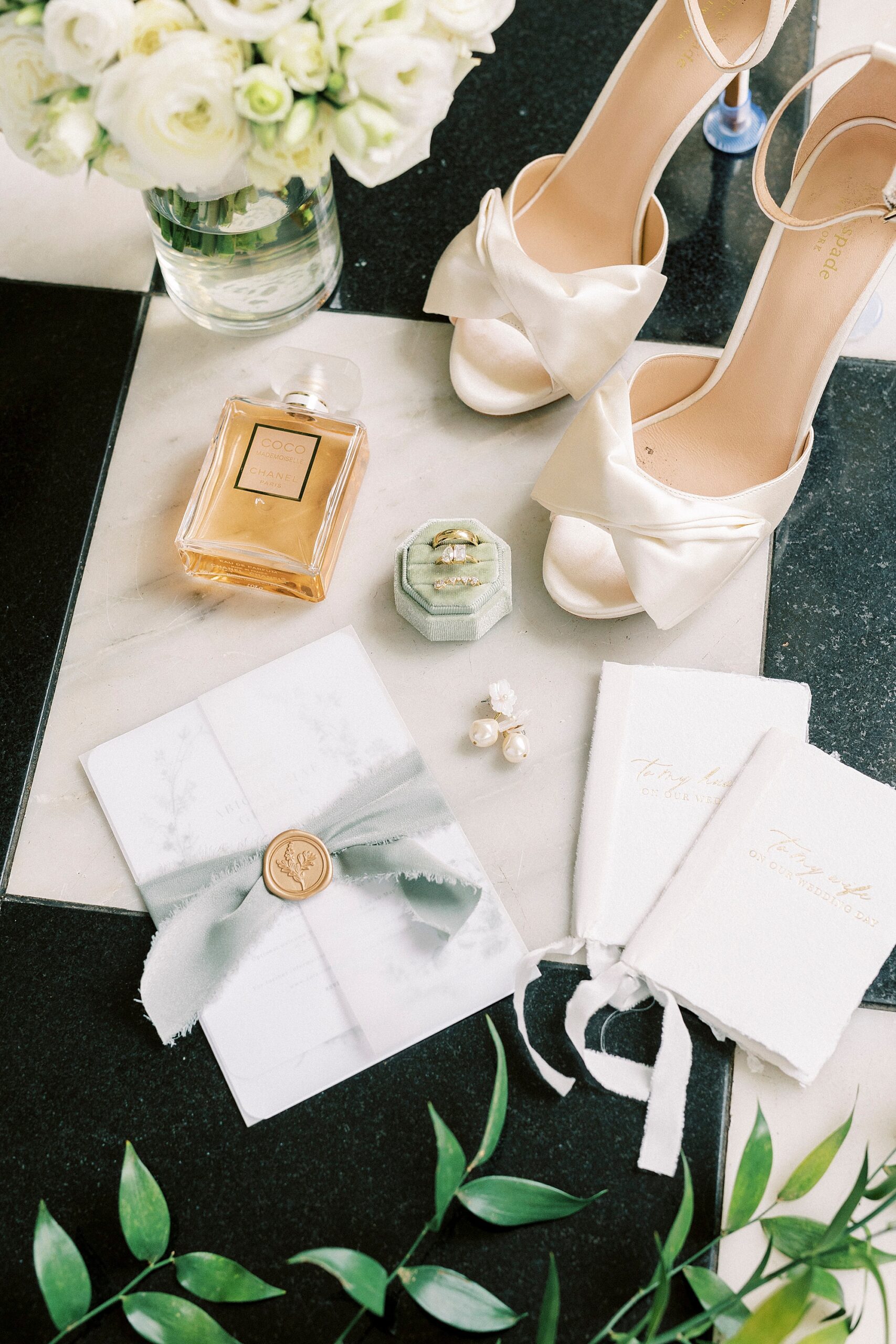 bride's white shoes, perfume, and jewelry on black and white floor
