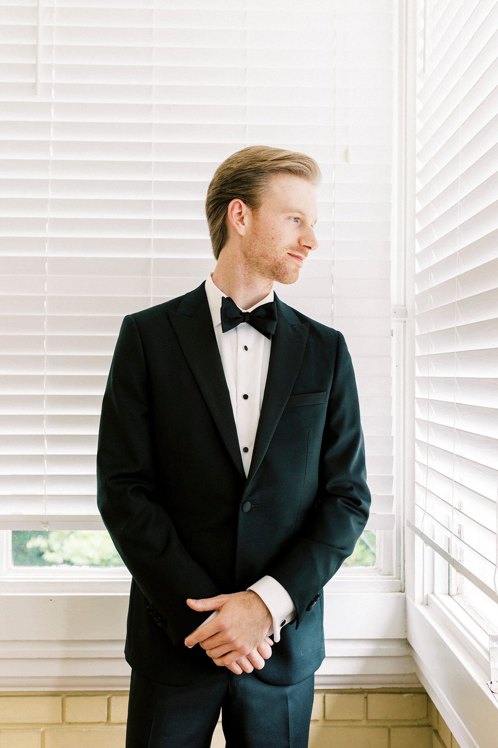 groom stands with hands in front of him looking out window of Separk Mansion