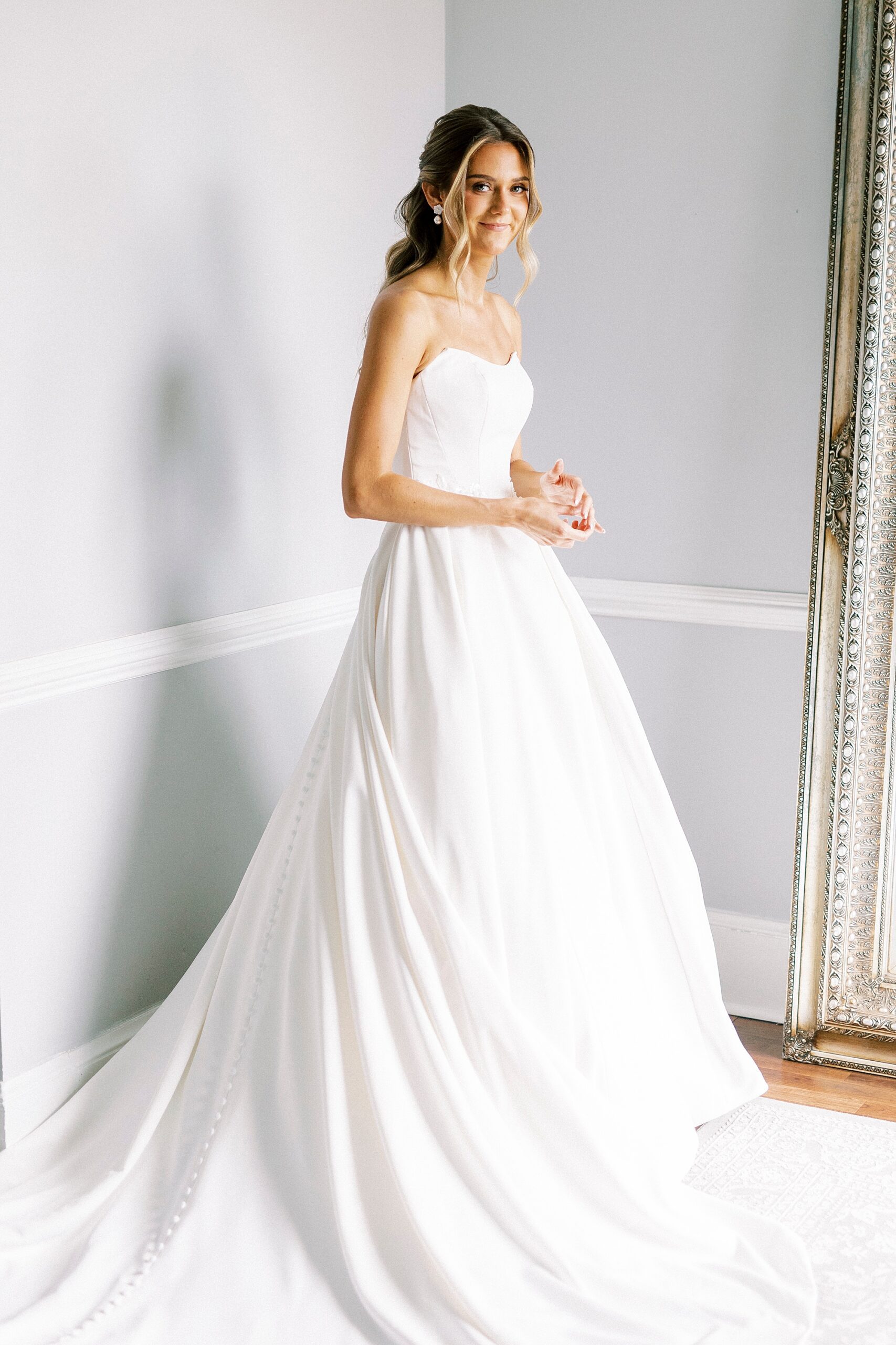 bride stands by mirror in suite in strapless wedding gown