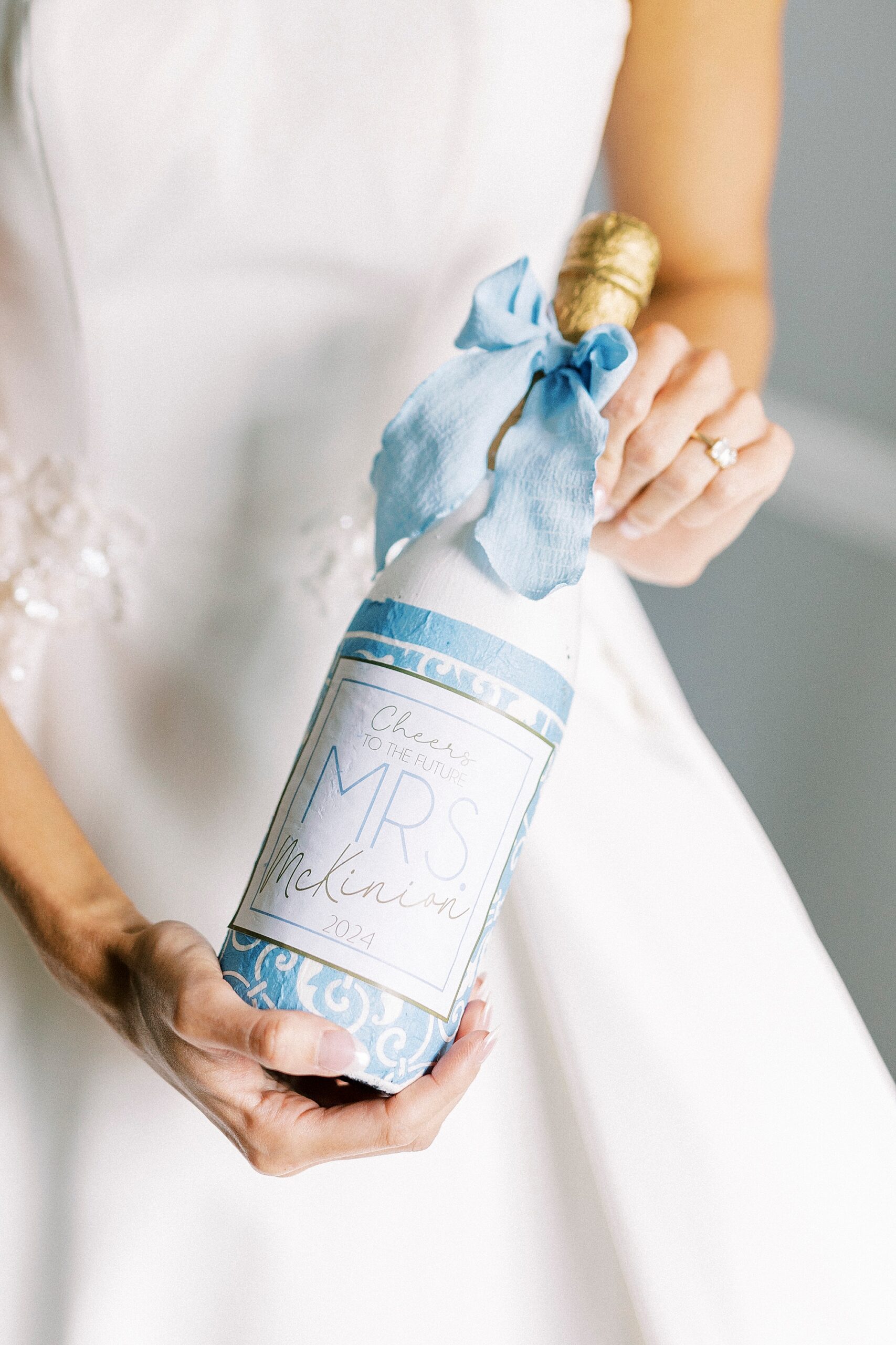 bride holds champagne bottle with blue ribbon and MRS label