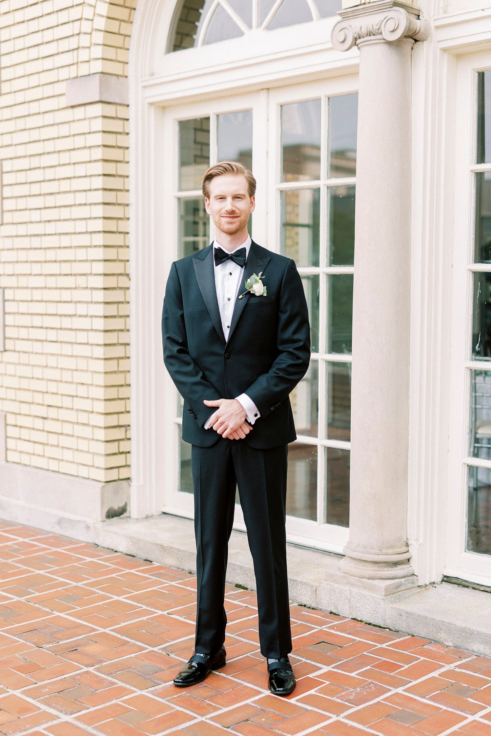 groom stands on brick patio in black suit at Separk Mansion