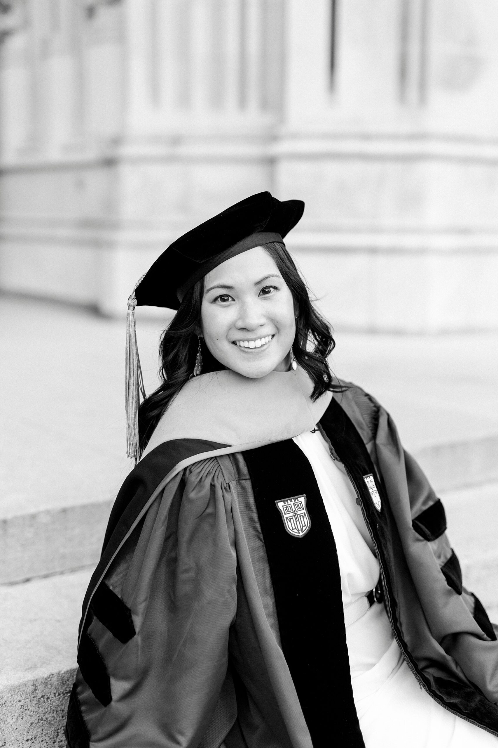 woman smiles leaning on step in robe and cap for graduation portraits