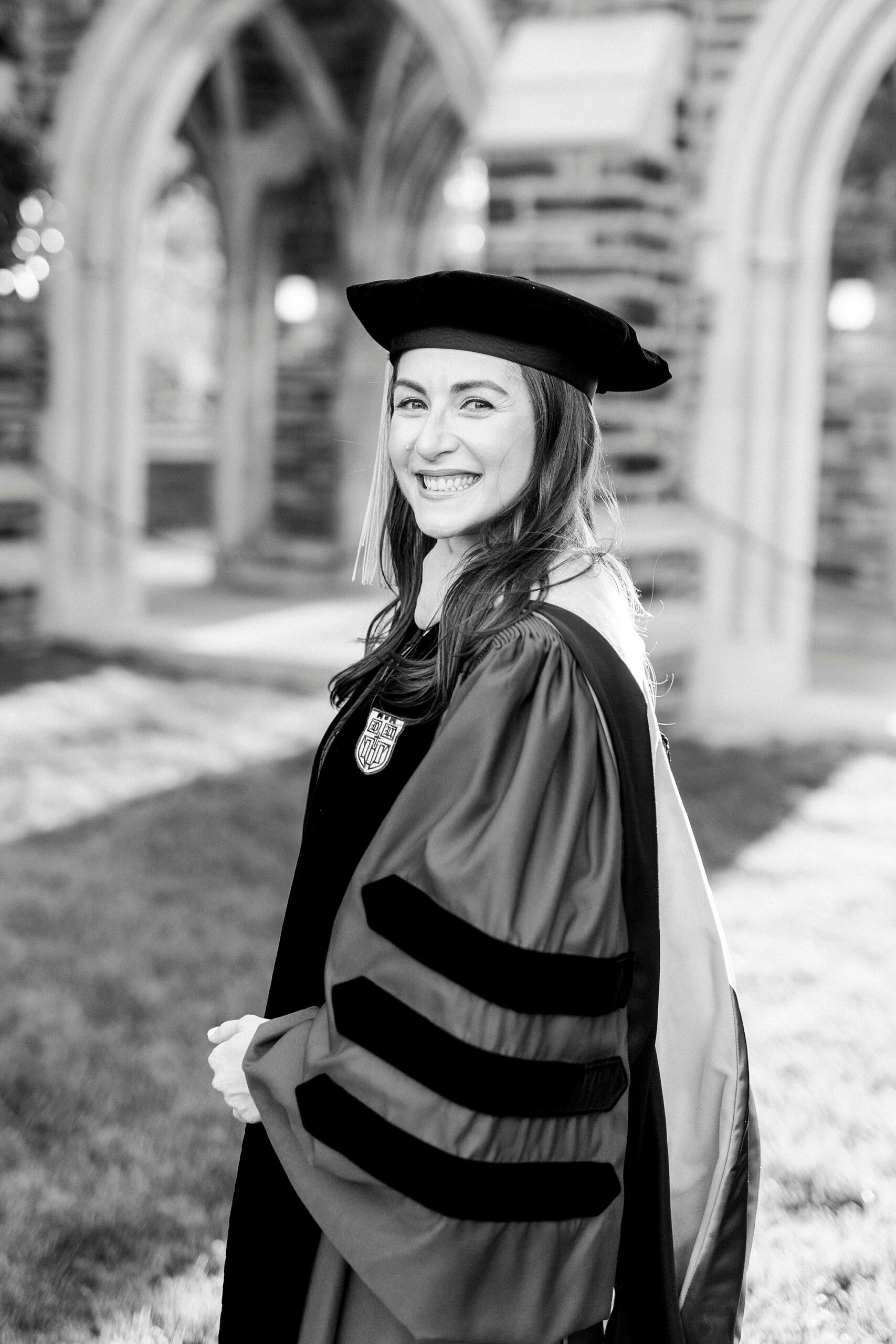 woman smiles over shoulder in graduate robe and hat at Duke University