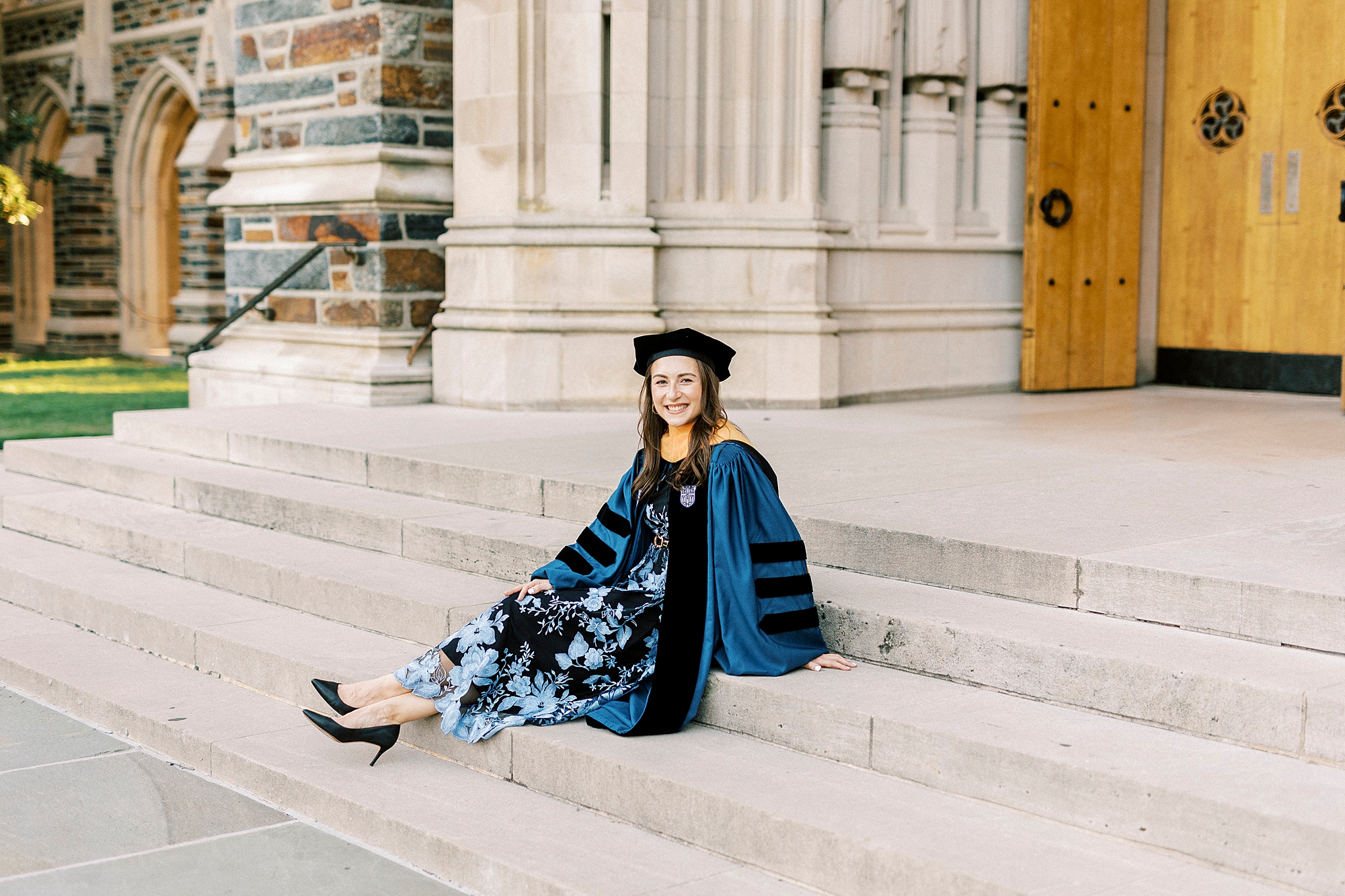 woman sits on steps in blue and black robe and hat at Duke University