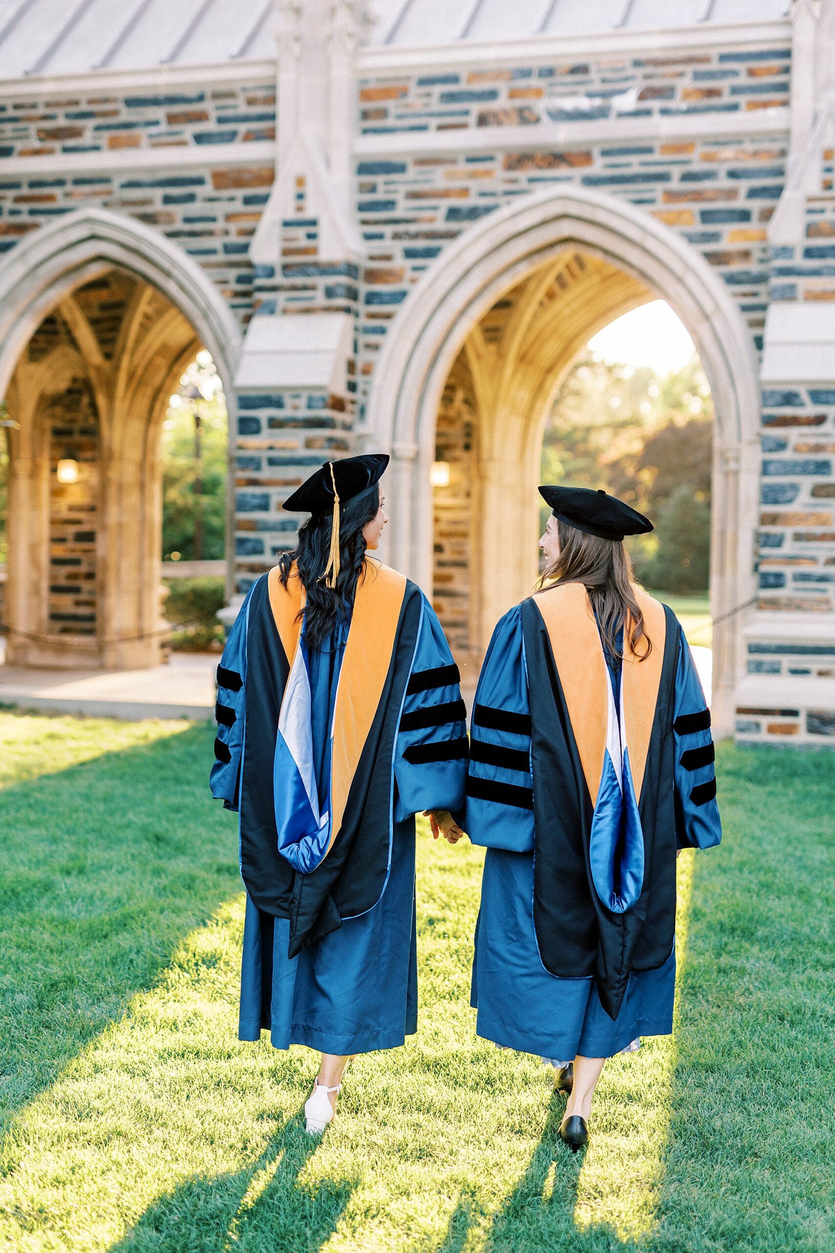 women in matching robes nad hats walk on lawn during Duke University graduation portraits