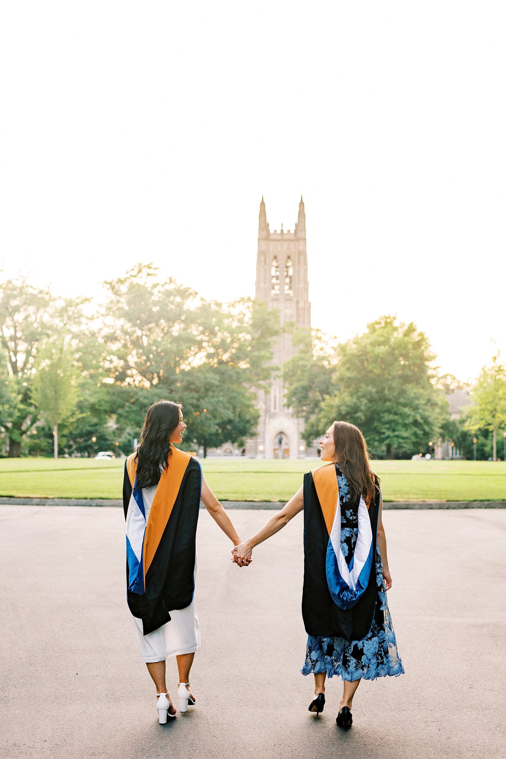 friends hold hands walking on campus towards bell tower at Duke University