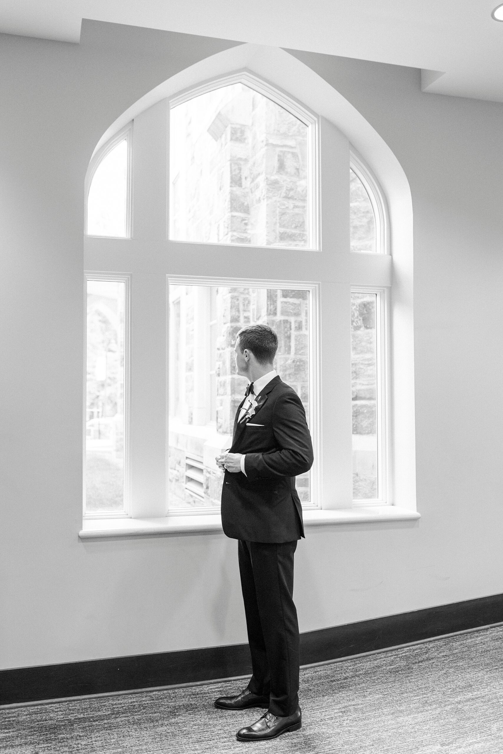 groom stands by window of chapel in Charlotte NC