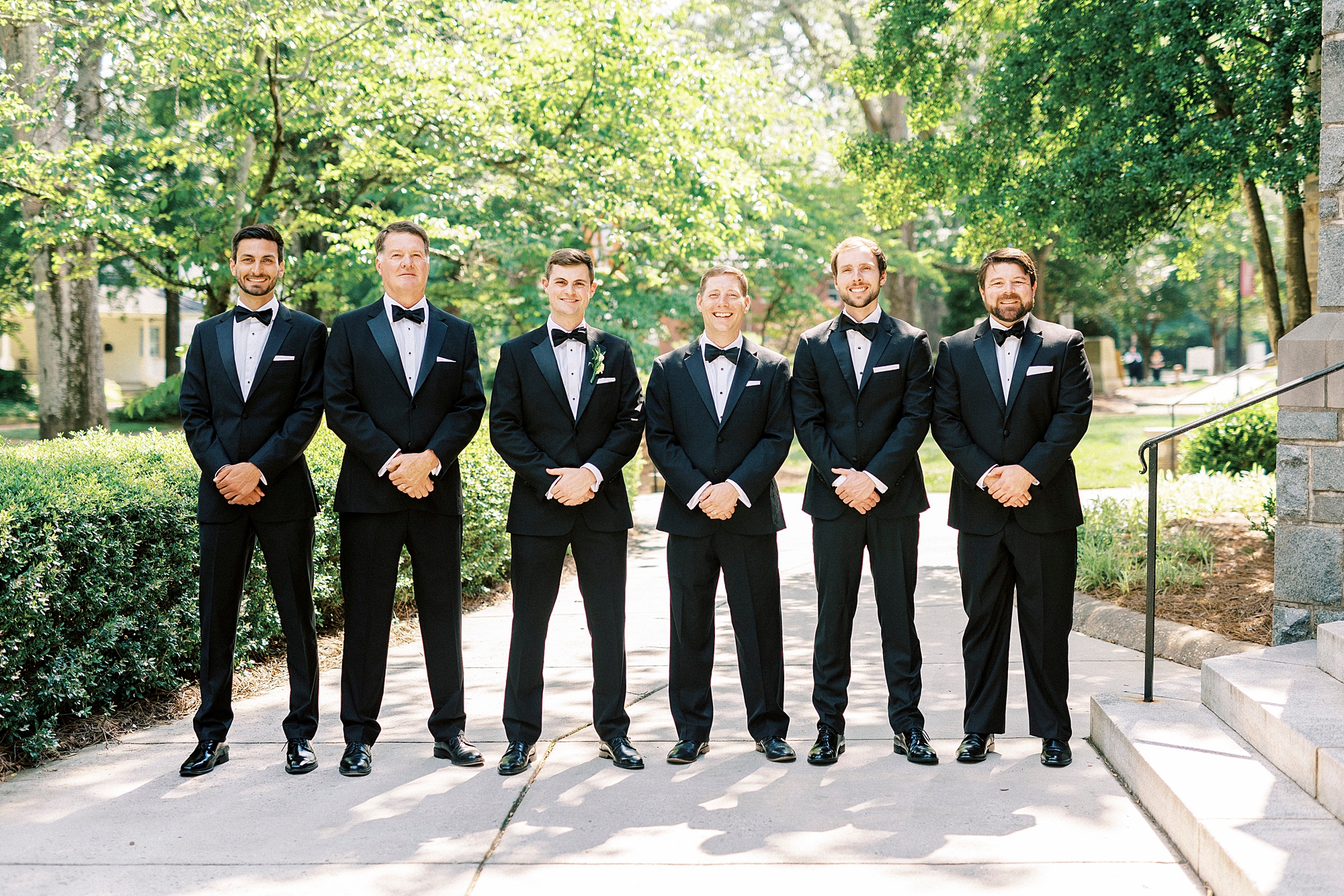 groom stands with groomsmen with arms in front of black suits