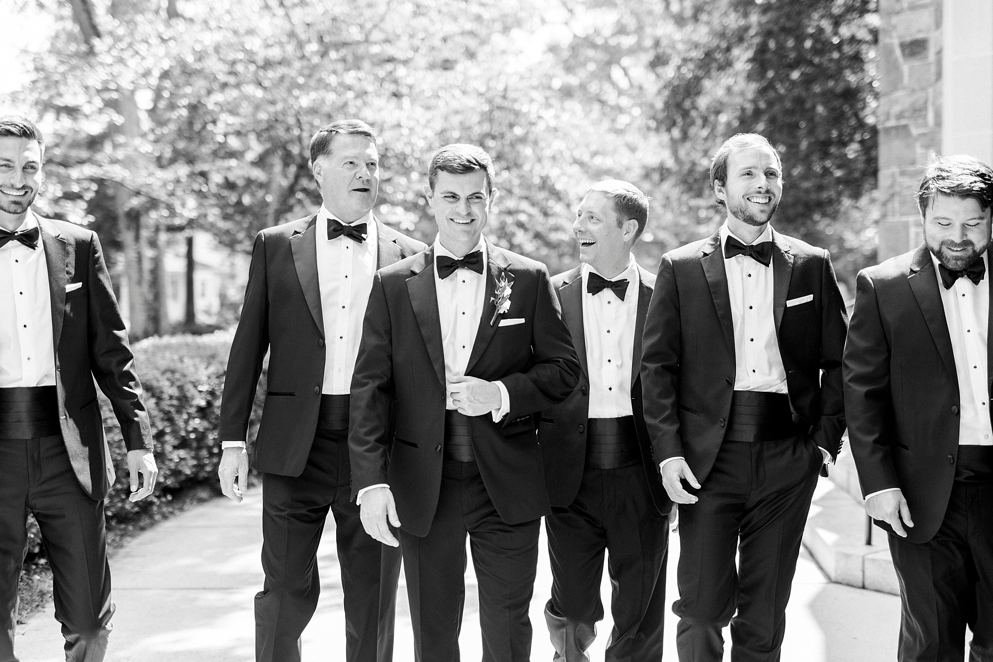 groom walks with groomsmen in black suits on side walk