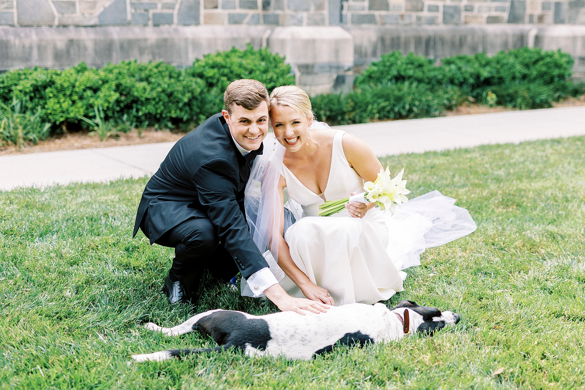 bride and groom kneel on grass outside Myers Presbyterian Church with dog