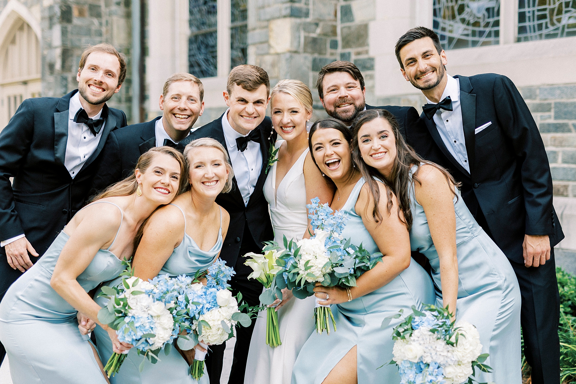 bride and groom pose with wedding party around them in black and blue attire