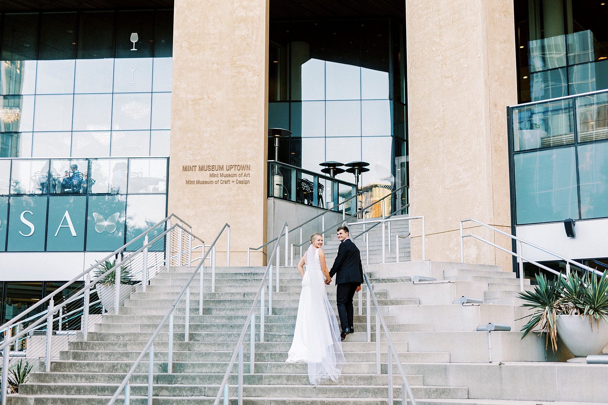 bride and groom walk up staircase outside the Mint Museum Uptown