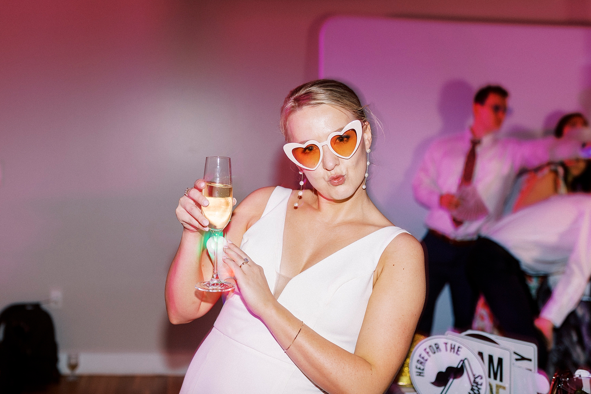 bride holds cocktail wearing heart shaped vintage sunglasses