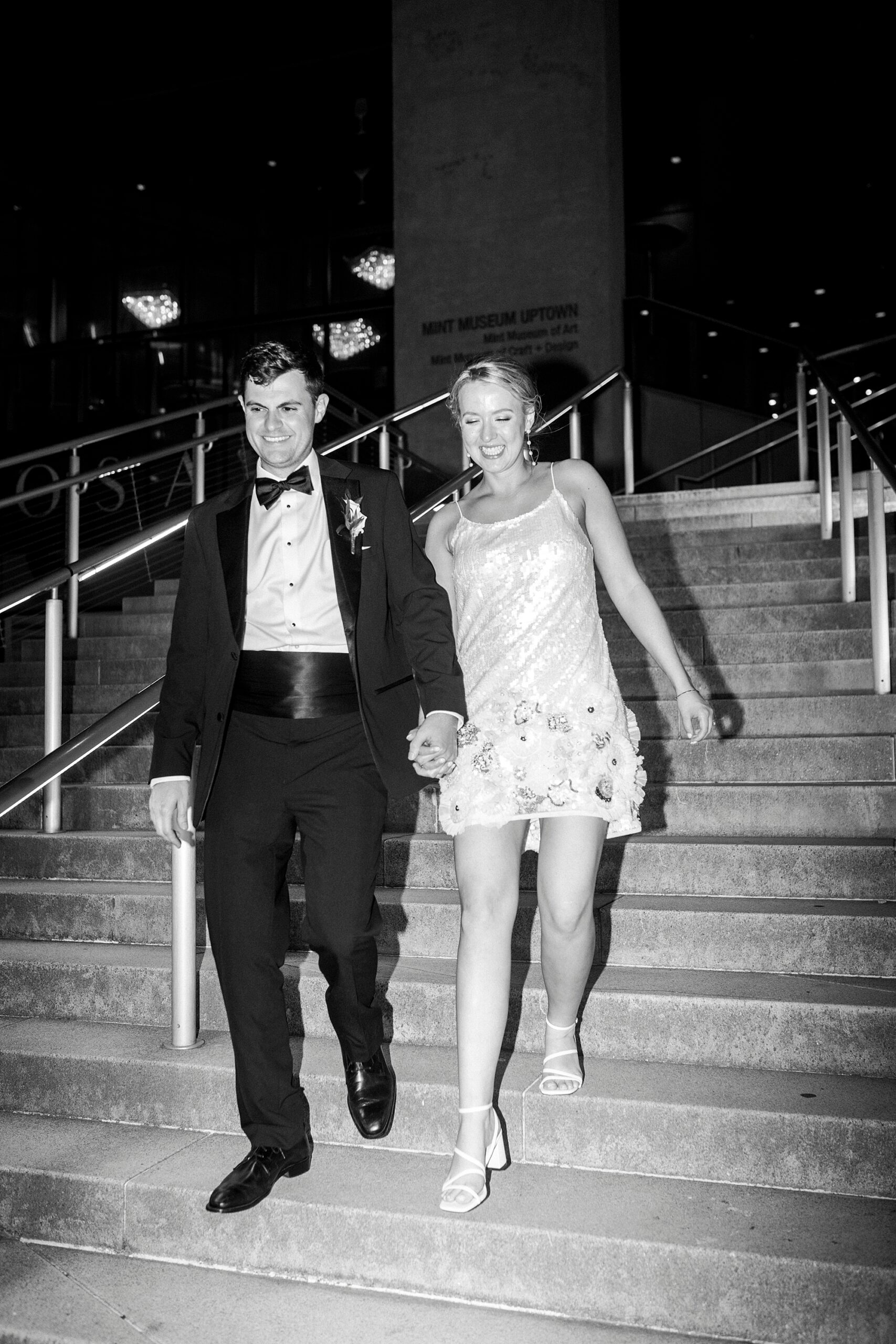 groom holds bride's hands walking down steps at the Mint Museum Uptown