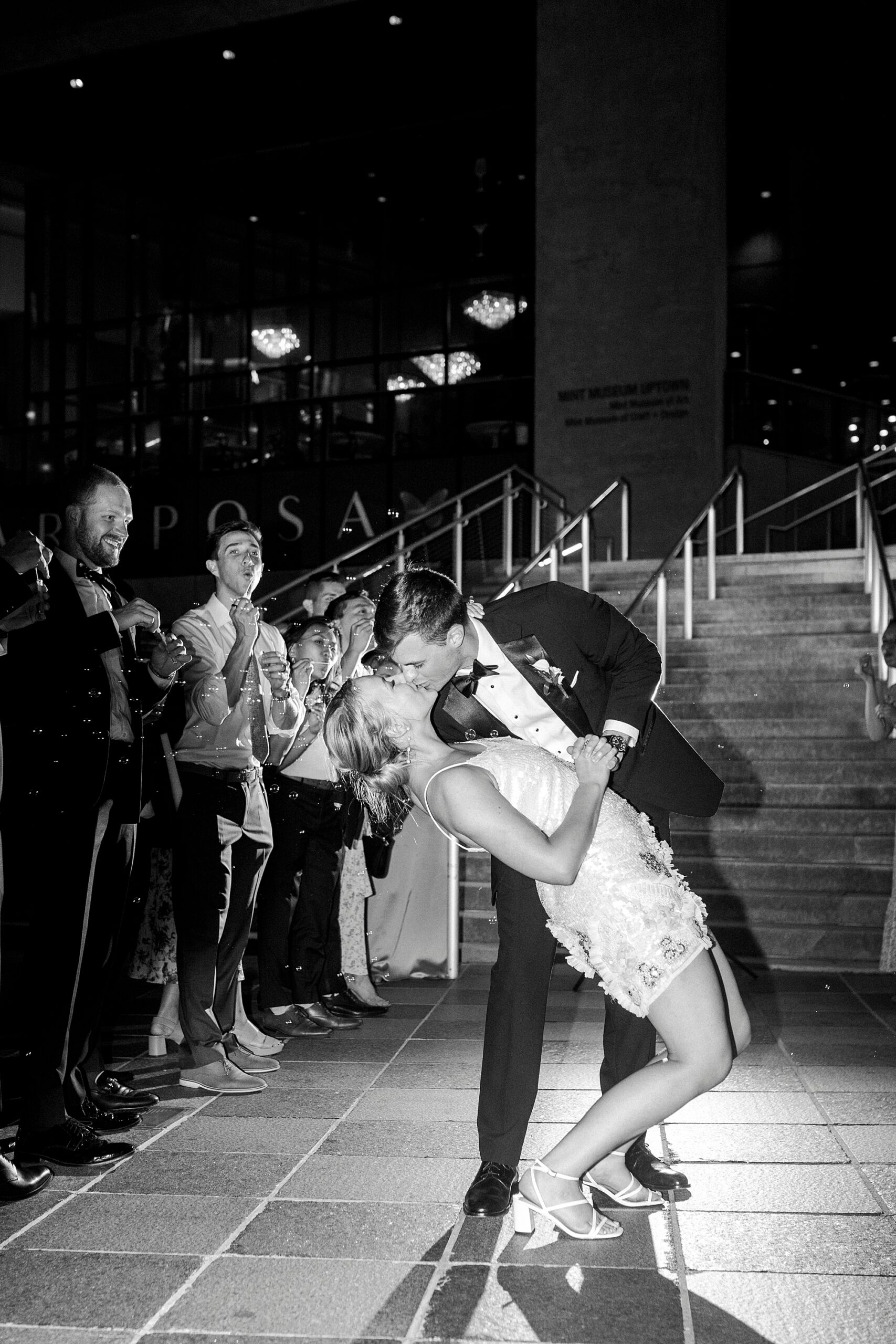 groom dips bride kissing her at base of staircase at the Mint Museum Uptown