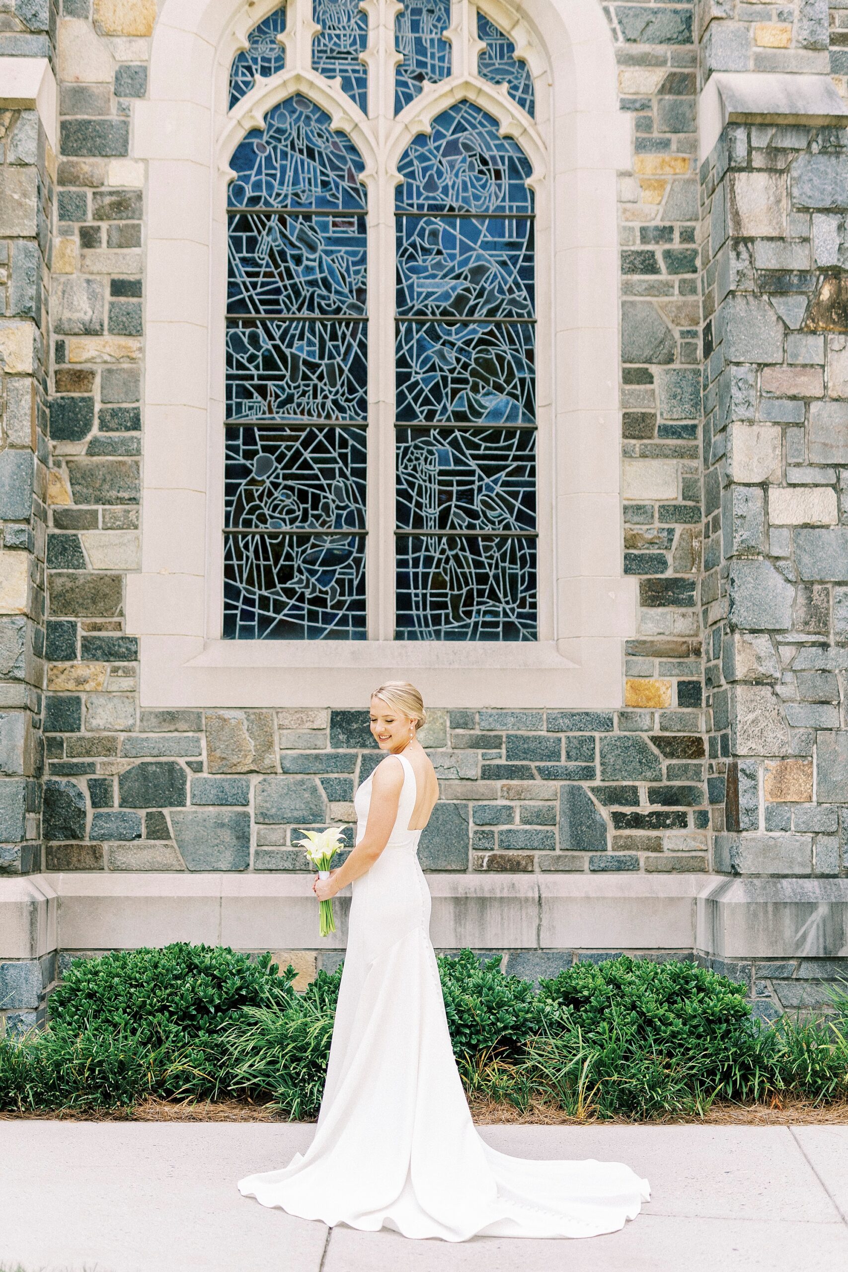 bride stands in front of stain glass window holding bouquet of white and blue flowers