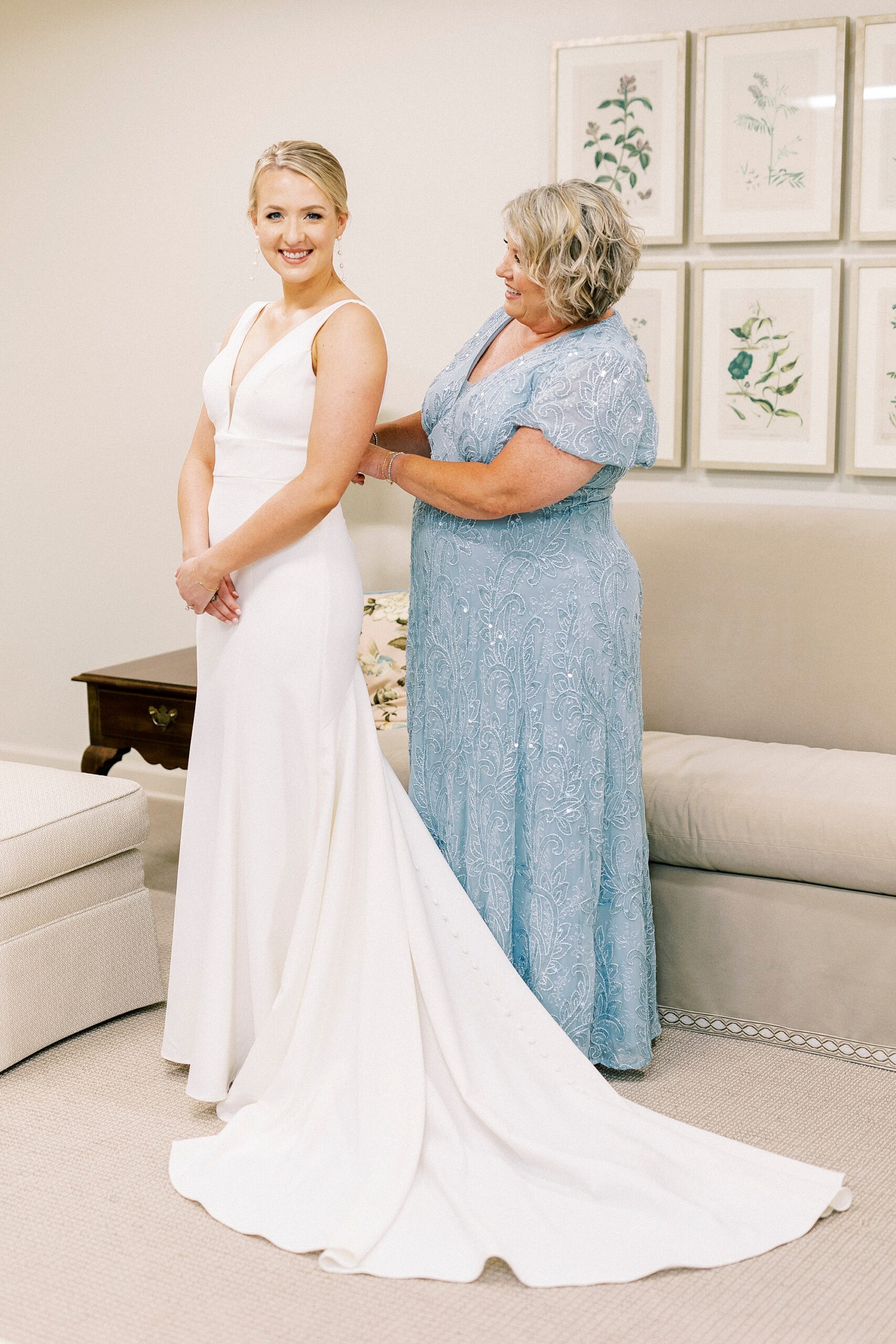 mother in blue dress helps bride into wedding gown