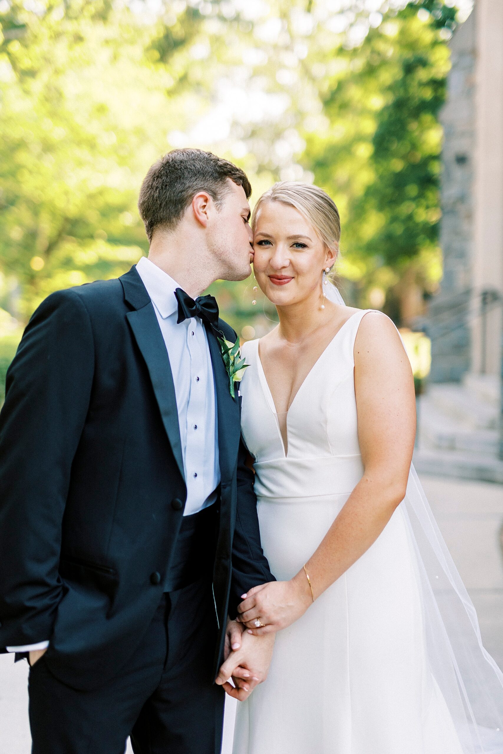 groom leans to kiss bride's cheek during wedding portraits