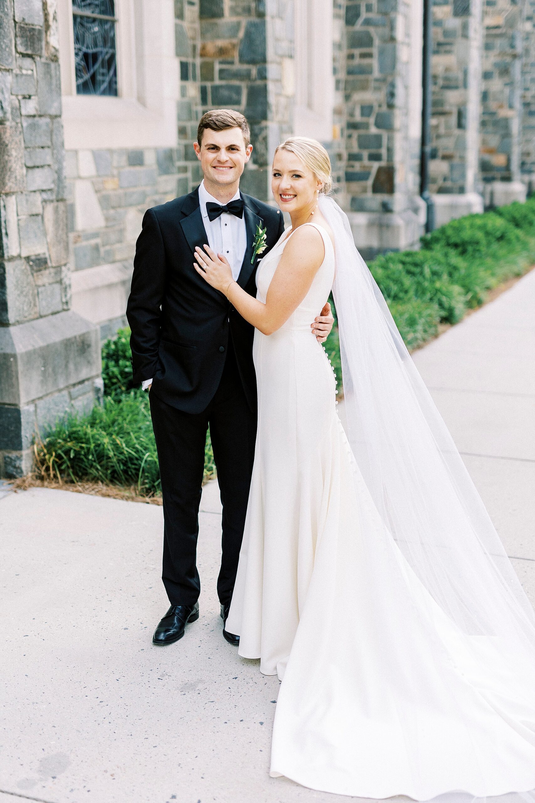 bride holds groom's suit lapel outside stone church