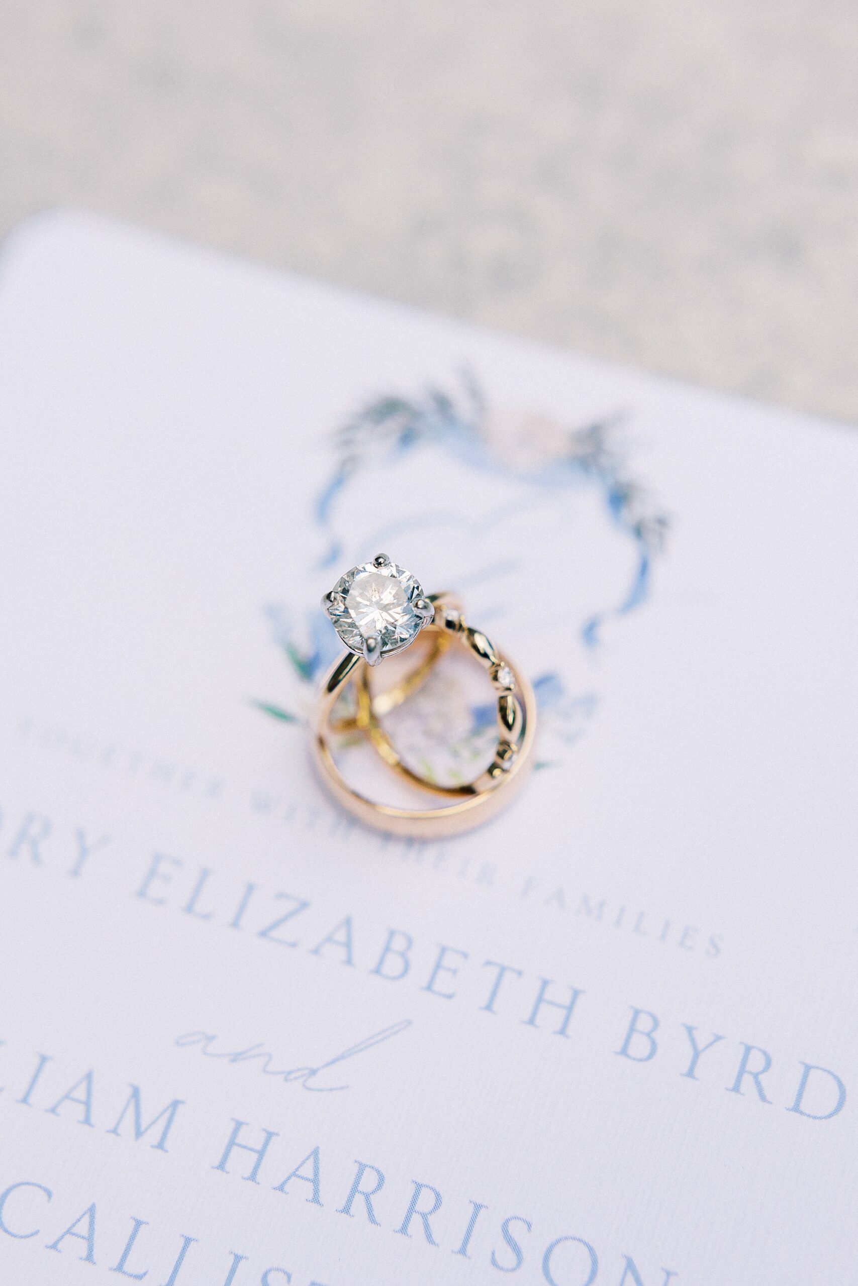 wedding bands rest on top of blue and white invitations for summer wedding