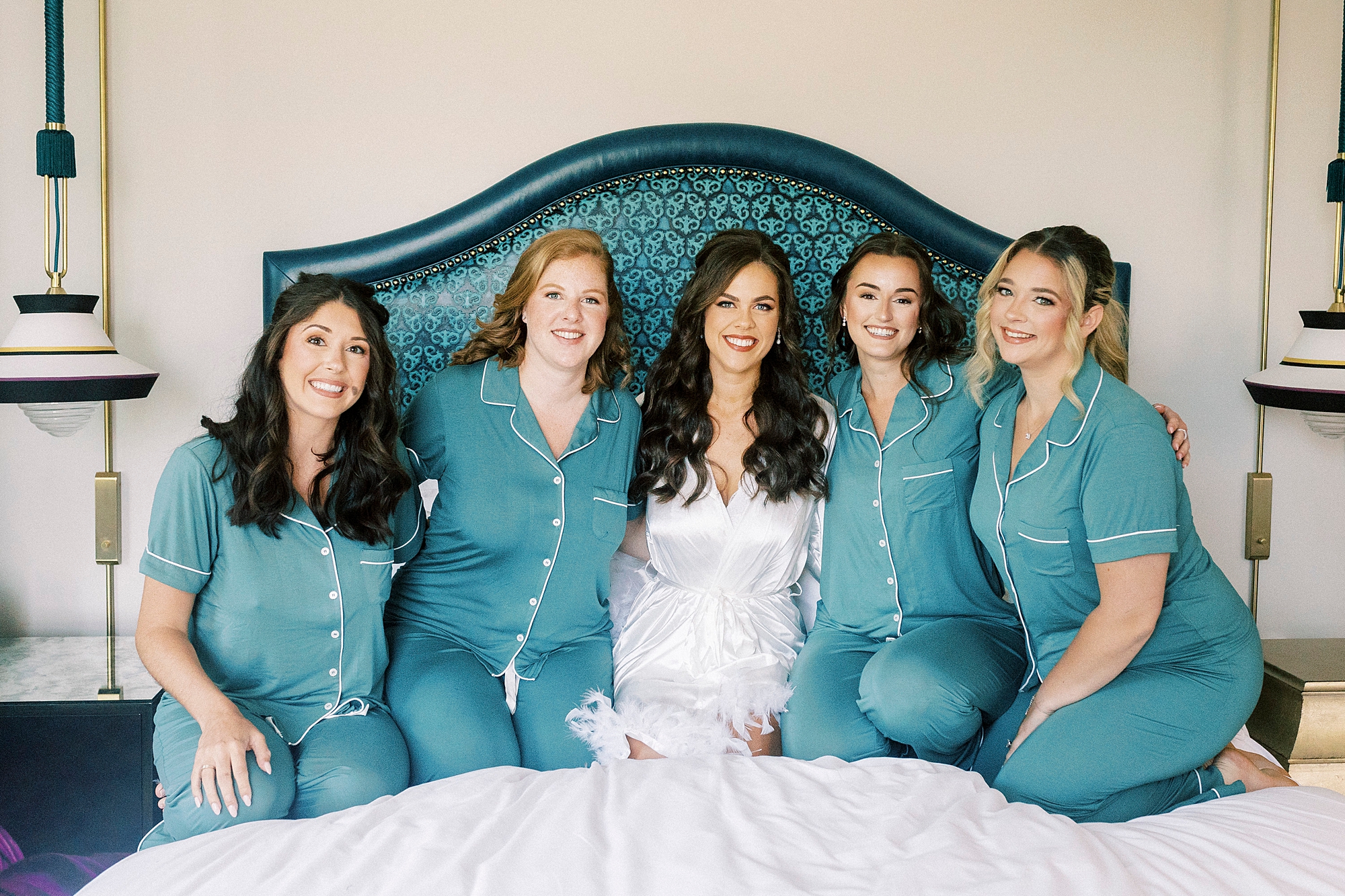 bride kneels on bed in matching pajamas with bridesmaids