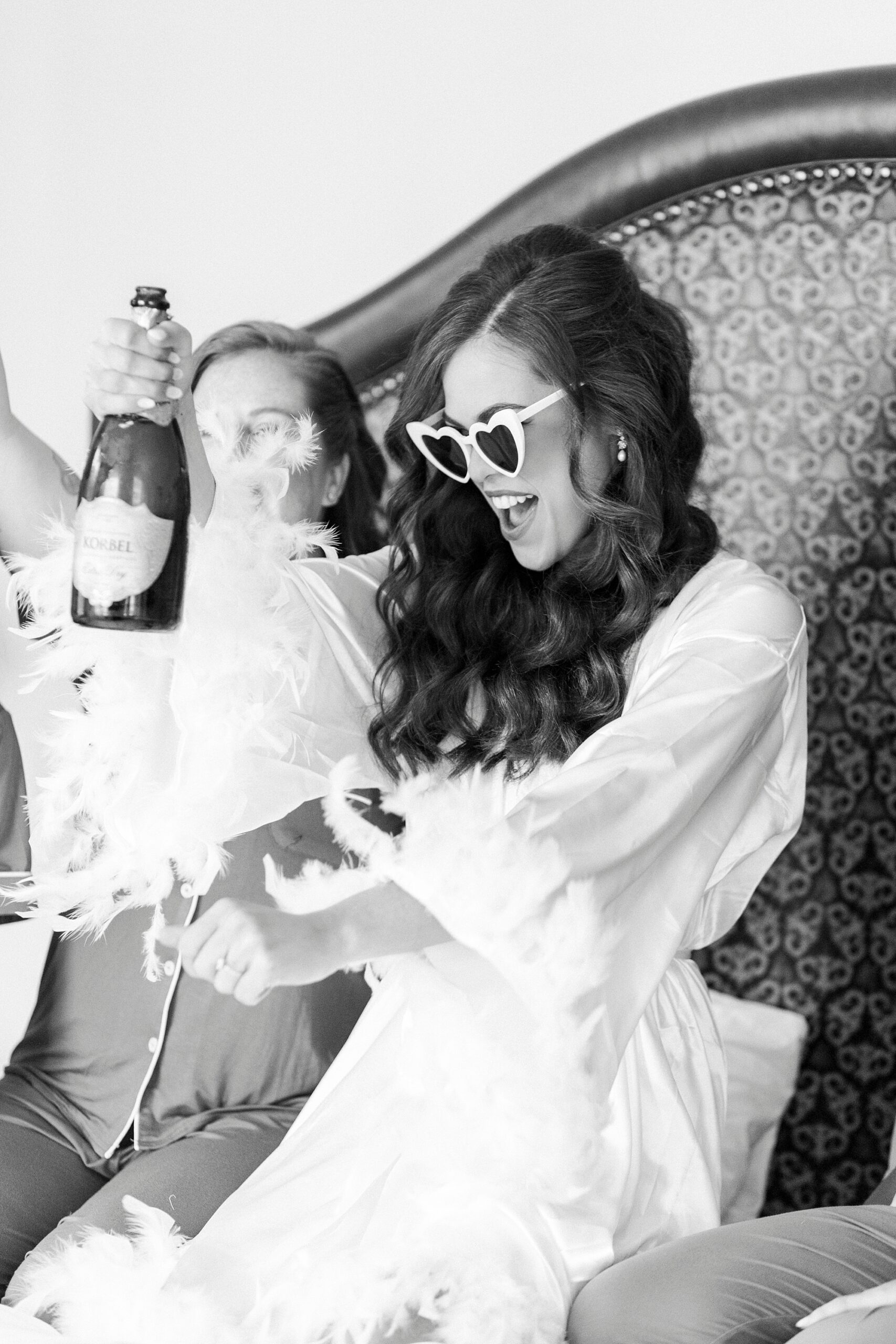 bride laughs holding bottle of champagne on bed of Charlotte hotel
