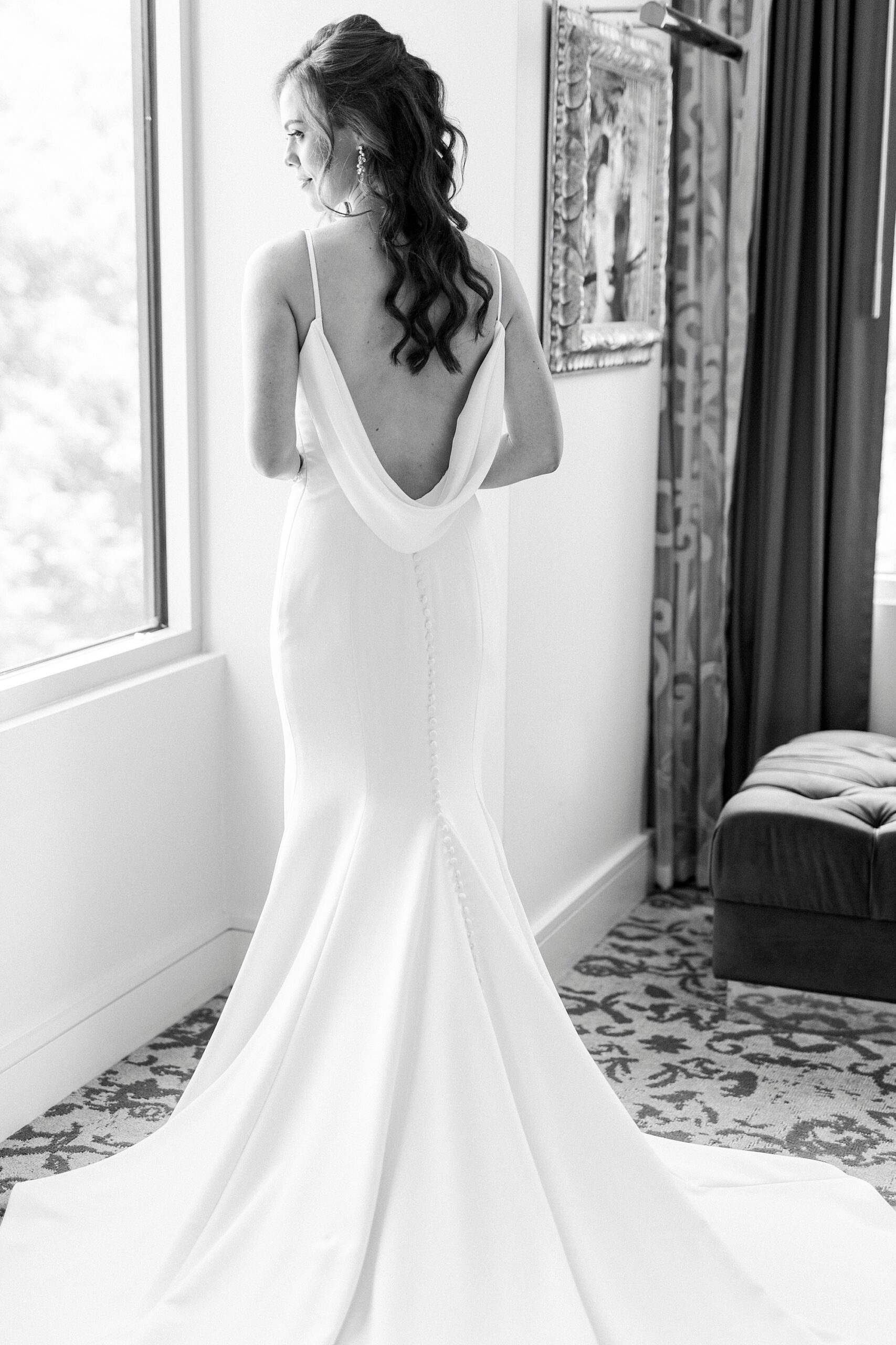 bride stands in window of hotel showing off draping on back of wedding gown
