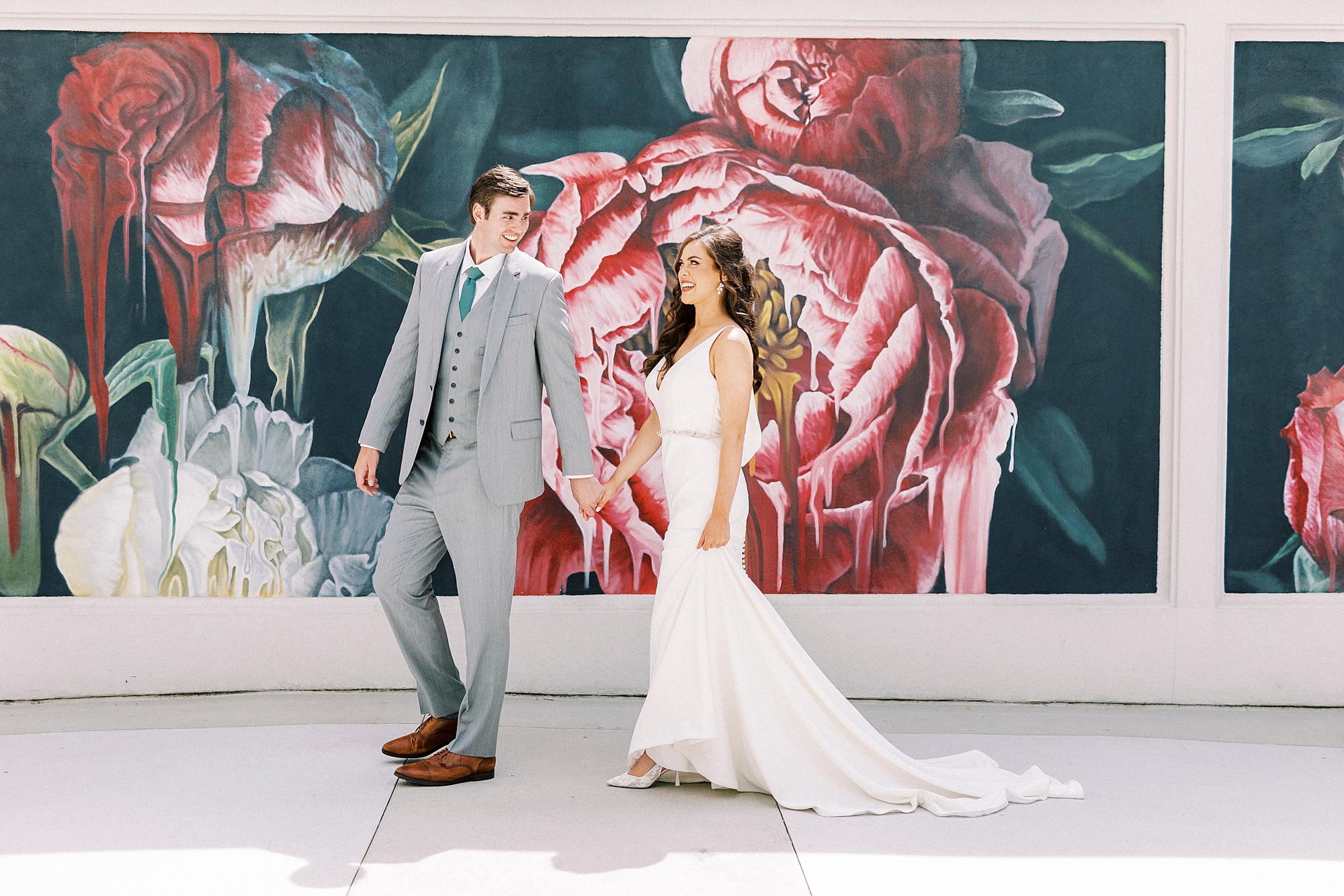 bride and groom hold hands in front of rose mural at the Grand Bohemian Hotel in Charlotte NC