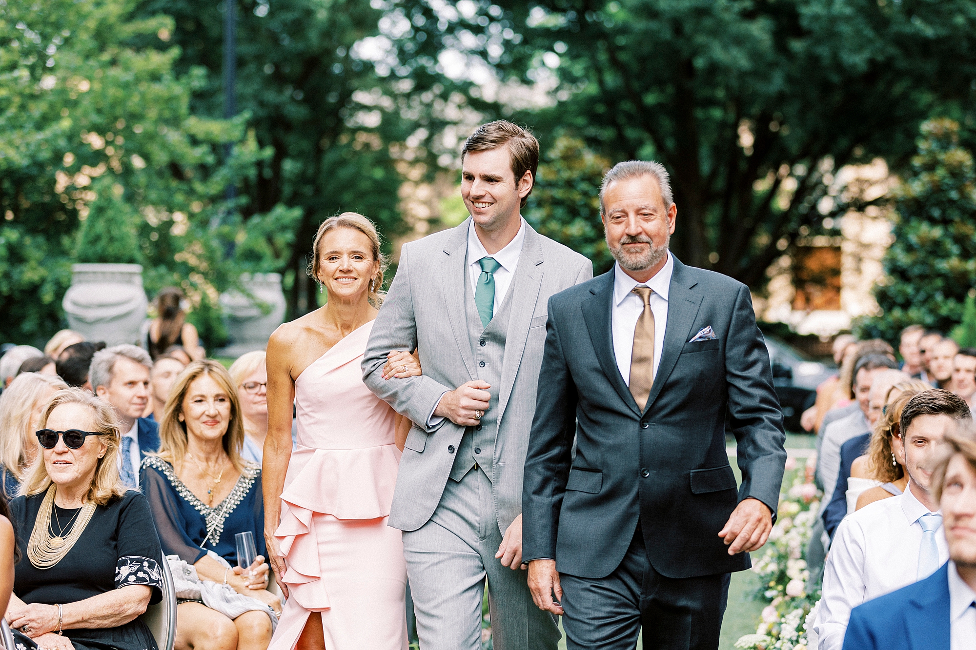 groom in grey suit walks with parents down aisle at the Grand Bohemian Hotel in Charlotte NC