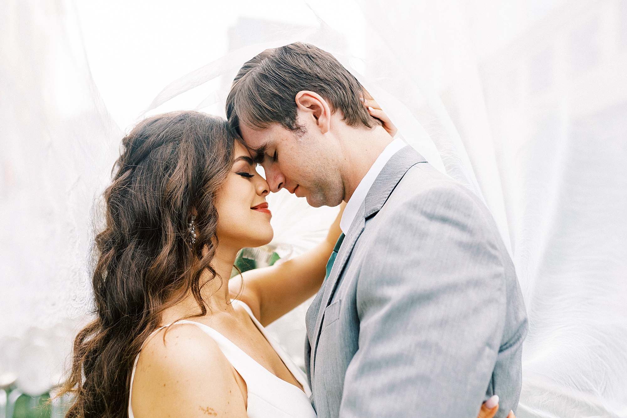 bride and groom hug under bride's veil smiling at each other