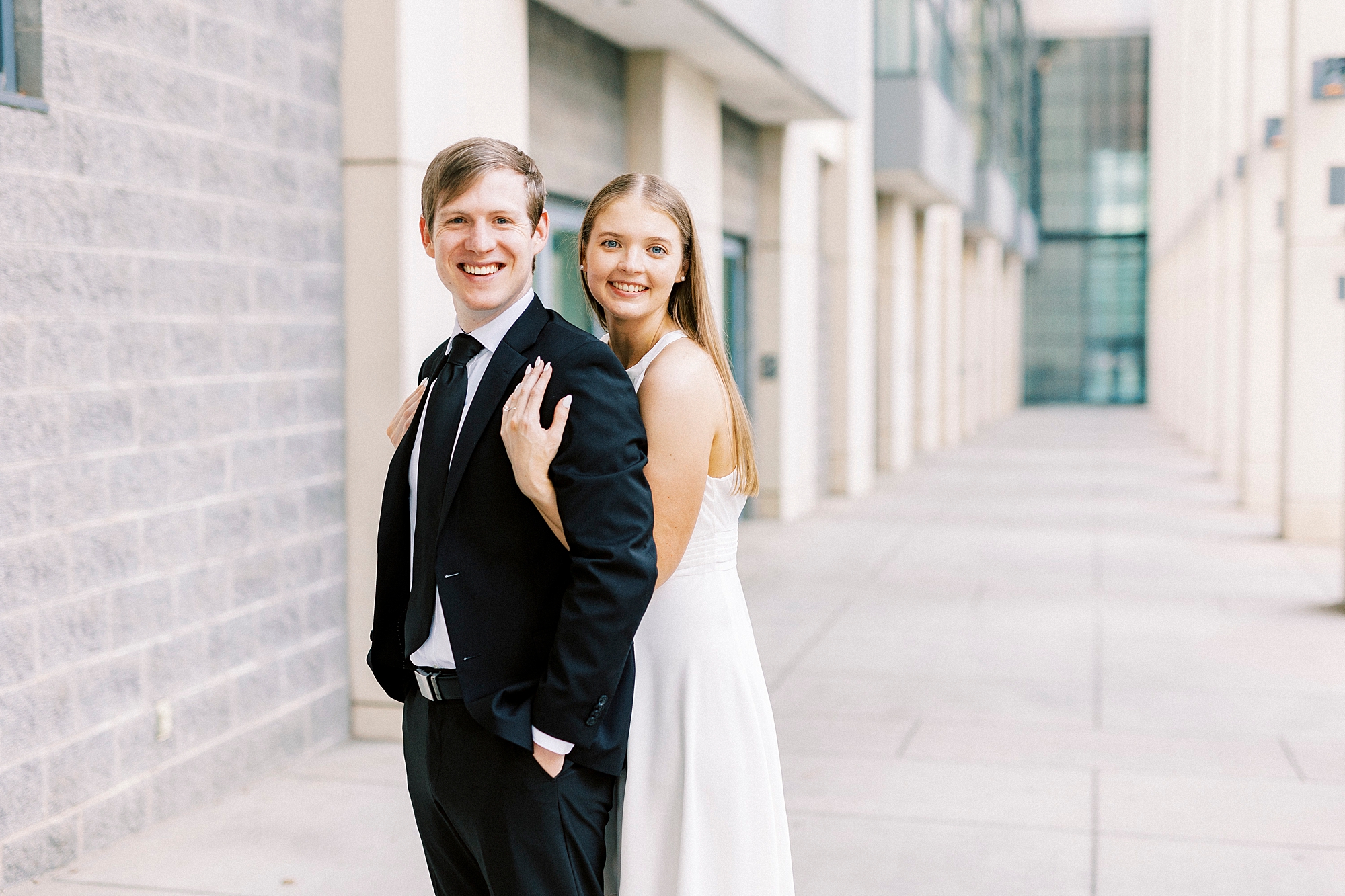 woman in white dress hugs man in black suit from behind at the Charlotte Convention Center