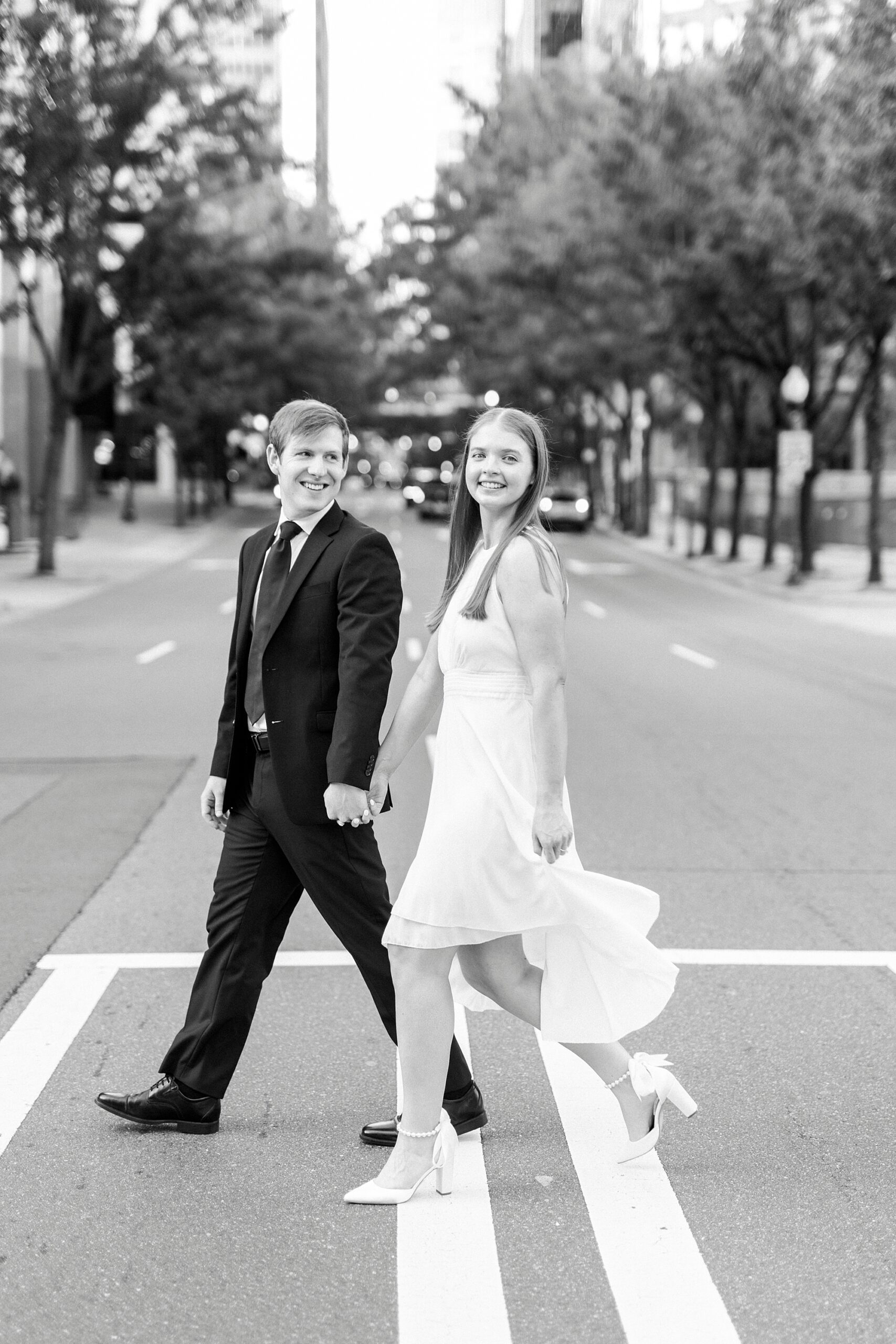 couple holds hands crossing street during chic Uptown Charlotte engagement session