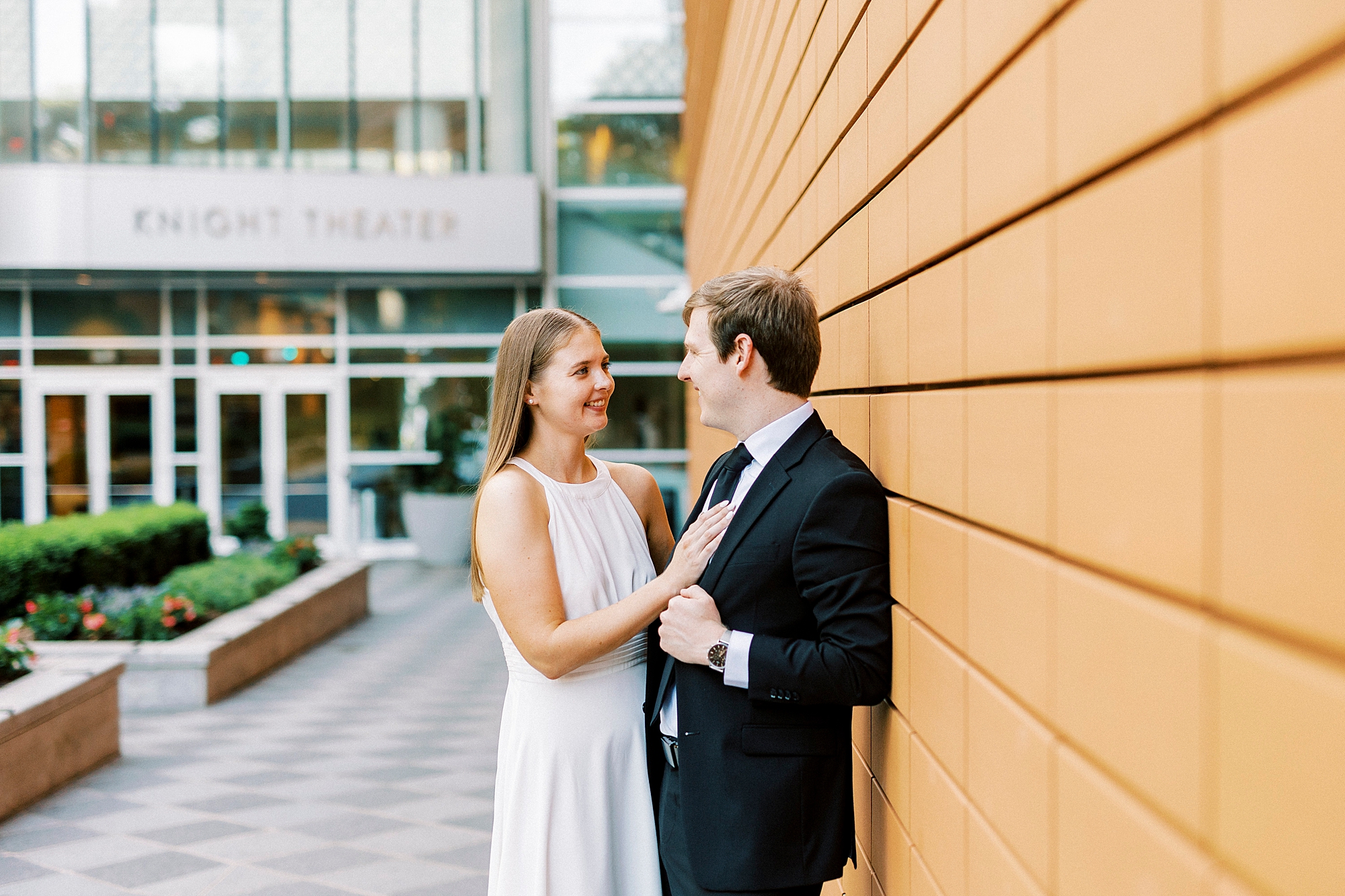 man leans against wall holding woman in white dress against him