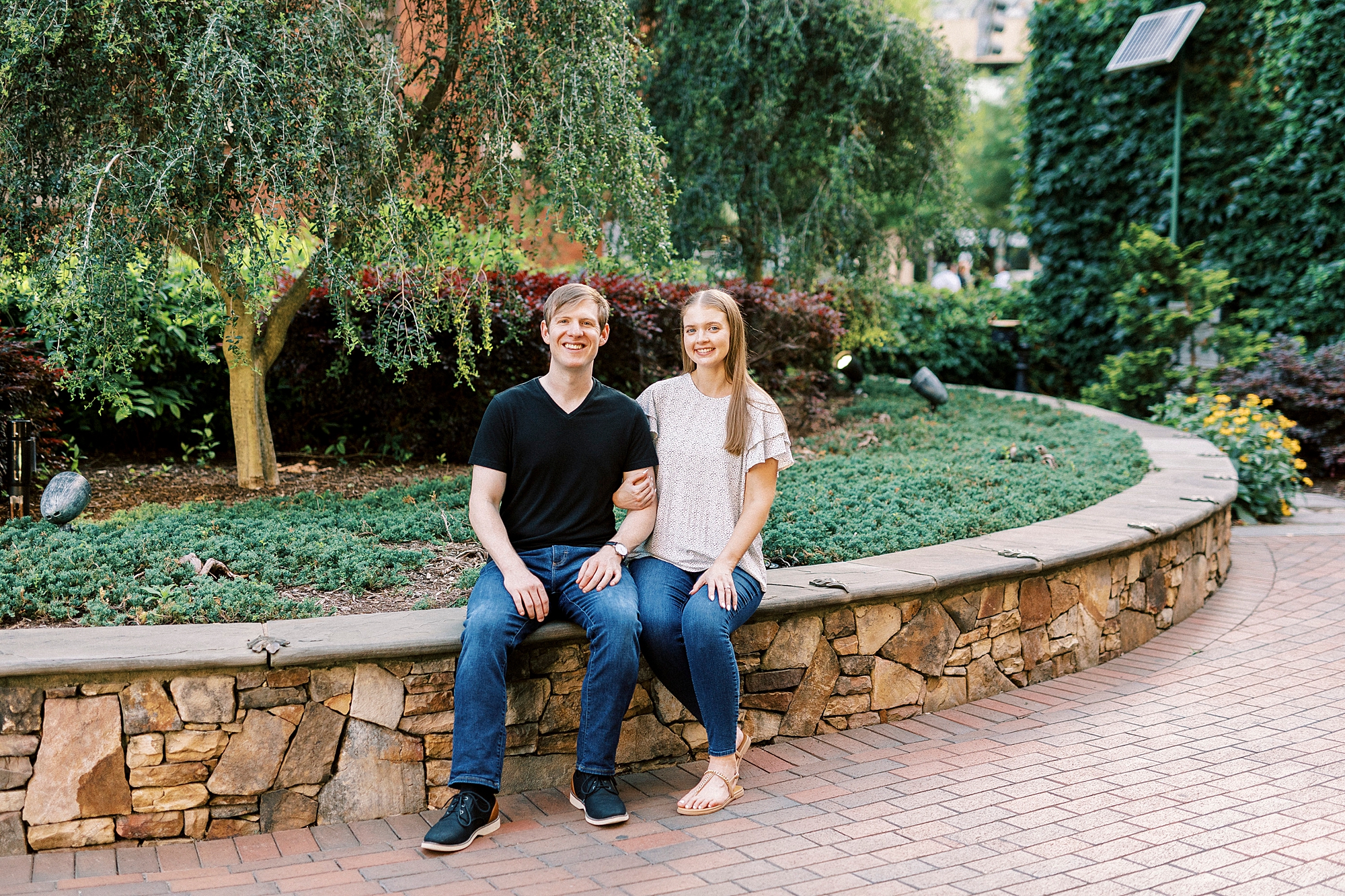 engaged couple sits on stone wall in Charlotte park