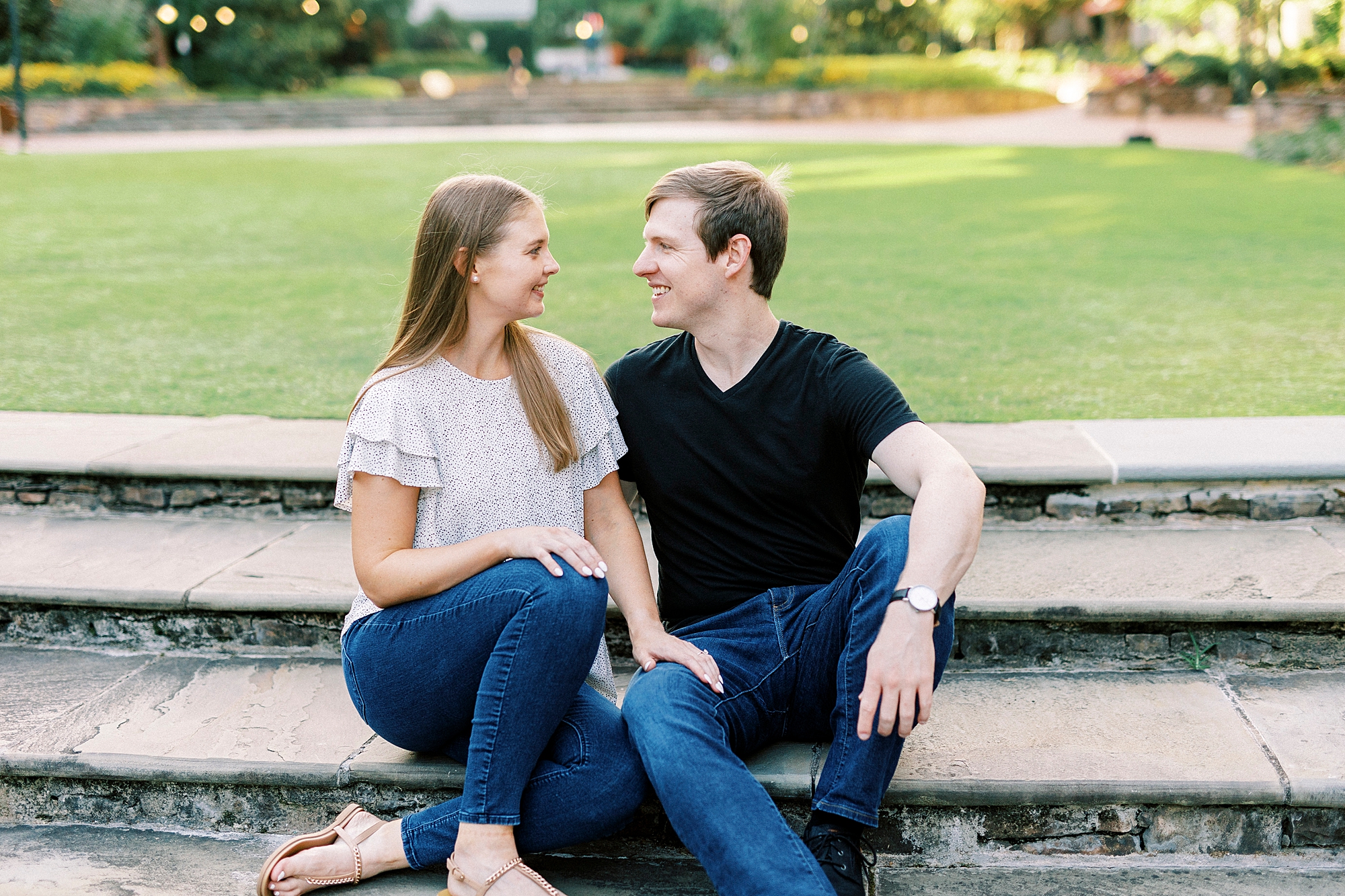 engaged couple sits in jeans and t-shirts in Charlotte green park