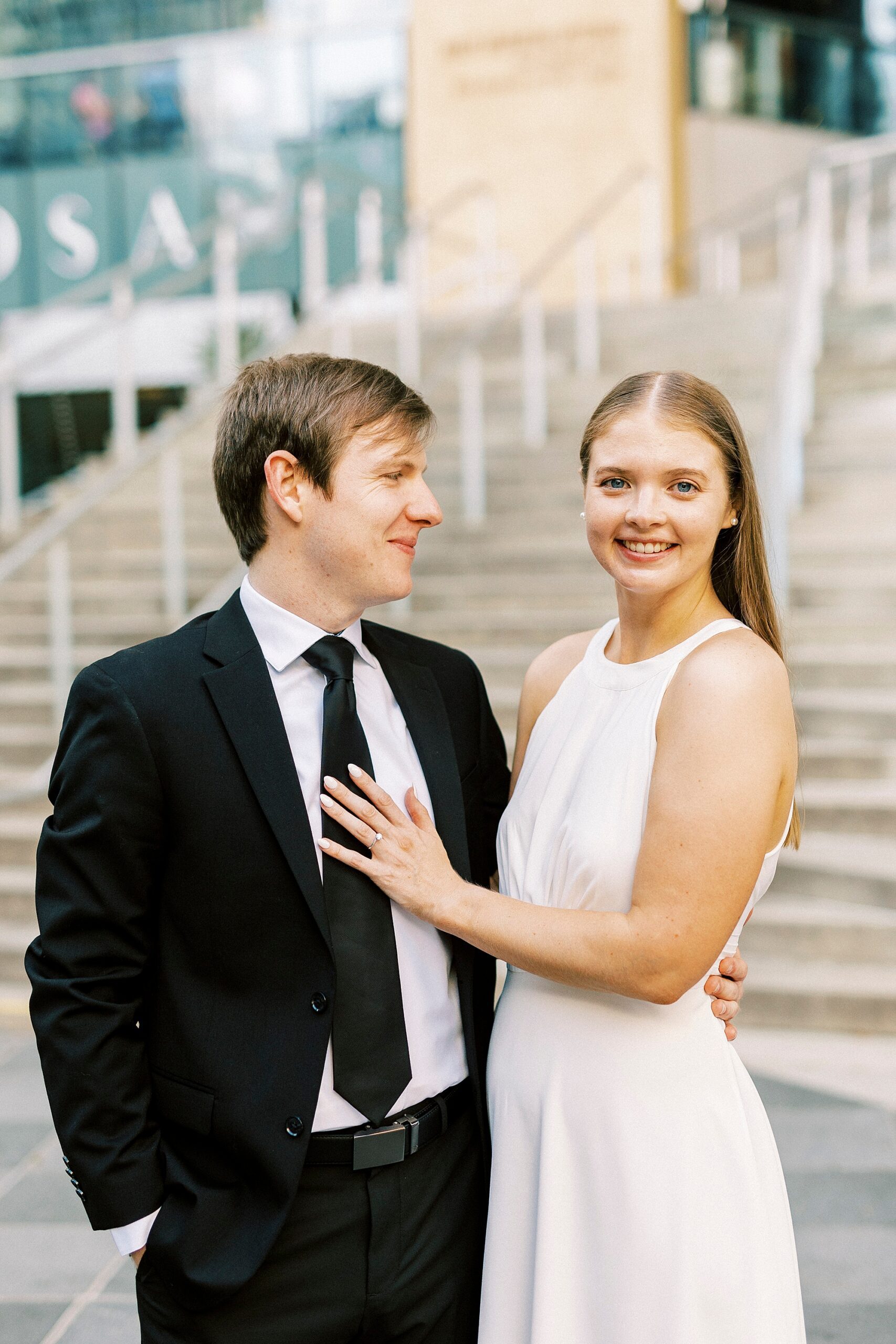 man in black suit looks at bride in white dress outside the Mint Museum 