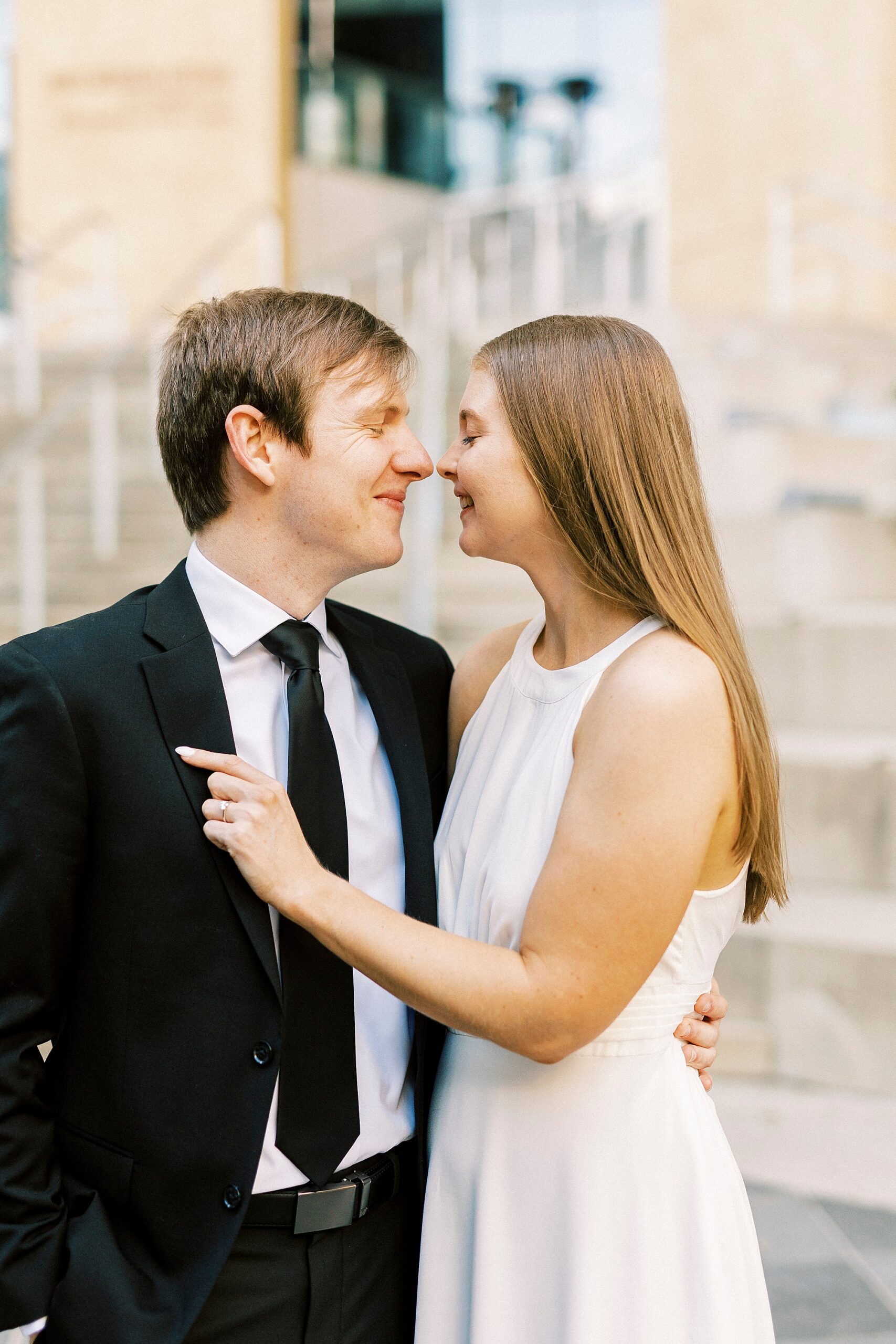 engaged couple stands nuzzling noses outside Charlotte museum 