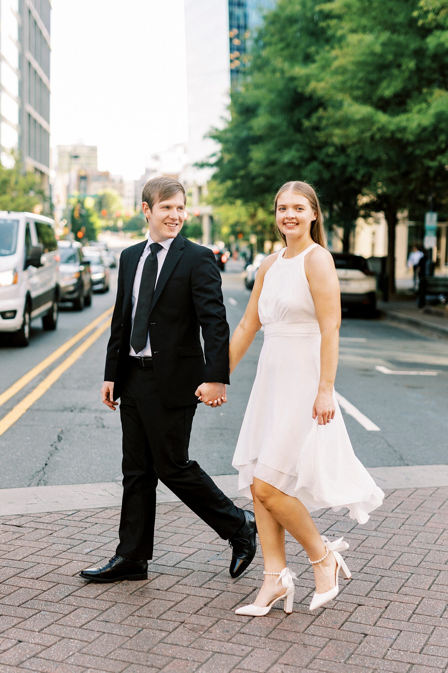engaged couple holds hands walking across crosswalk in uptown Charlotte