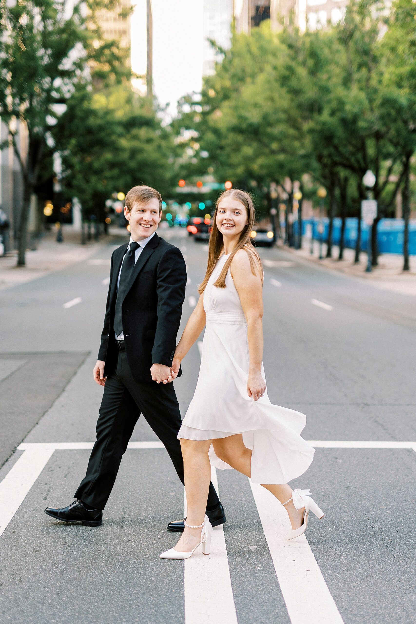 man holds woman's hand as they cross street in Uptown Charlotte NC