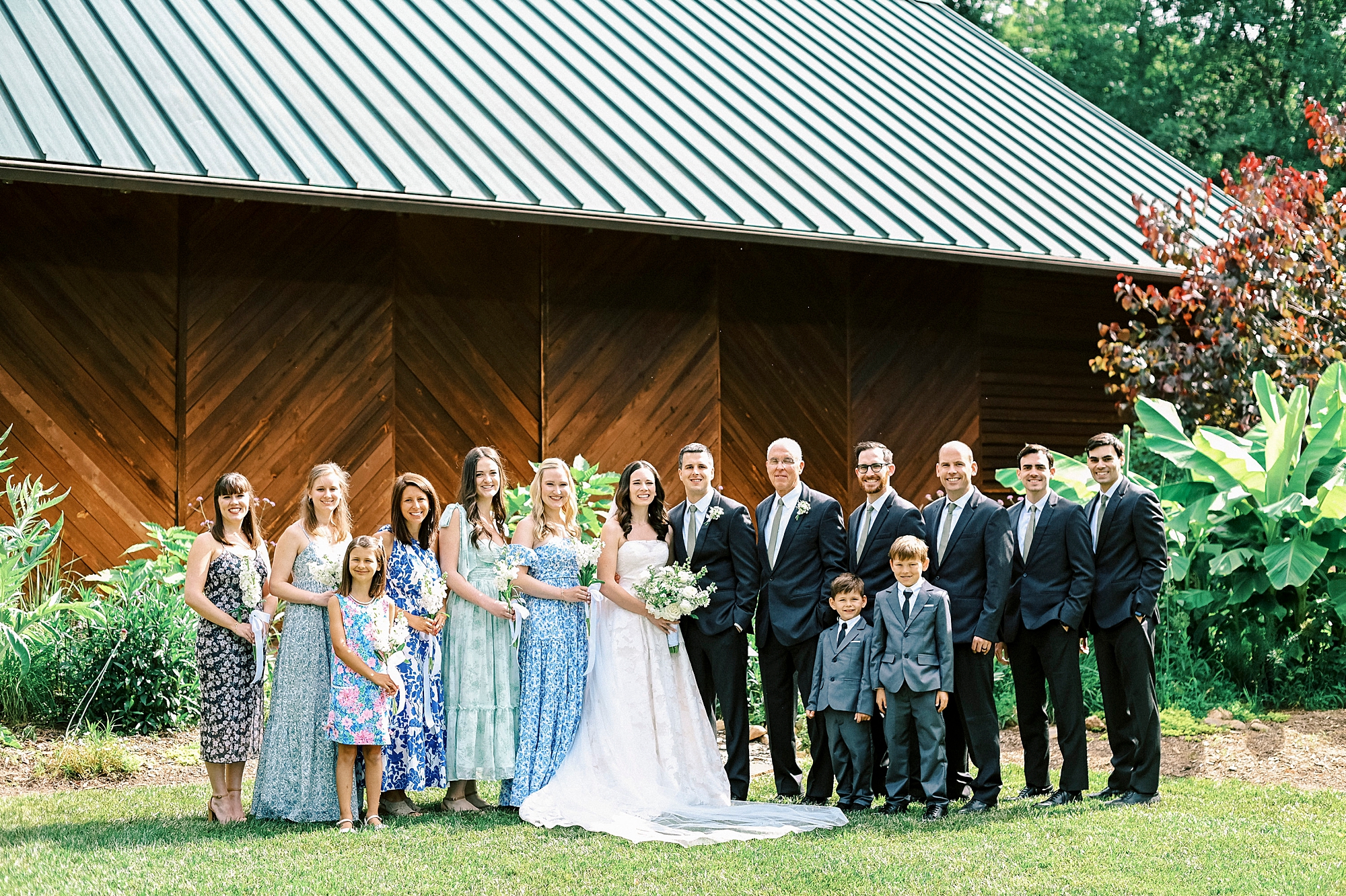 bride and groom pose with wedding party outside Alexander Homestead barn