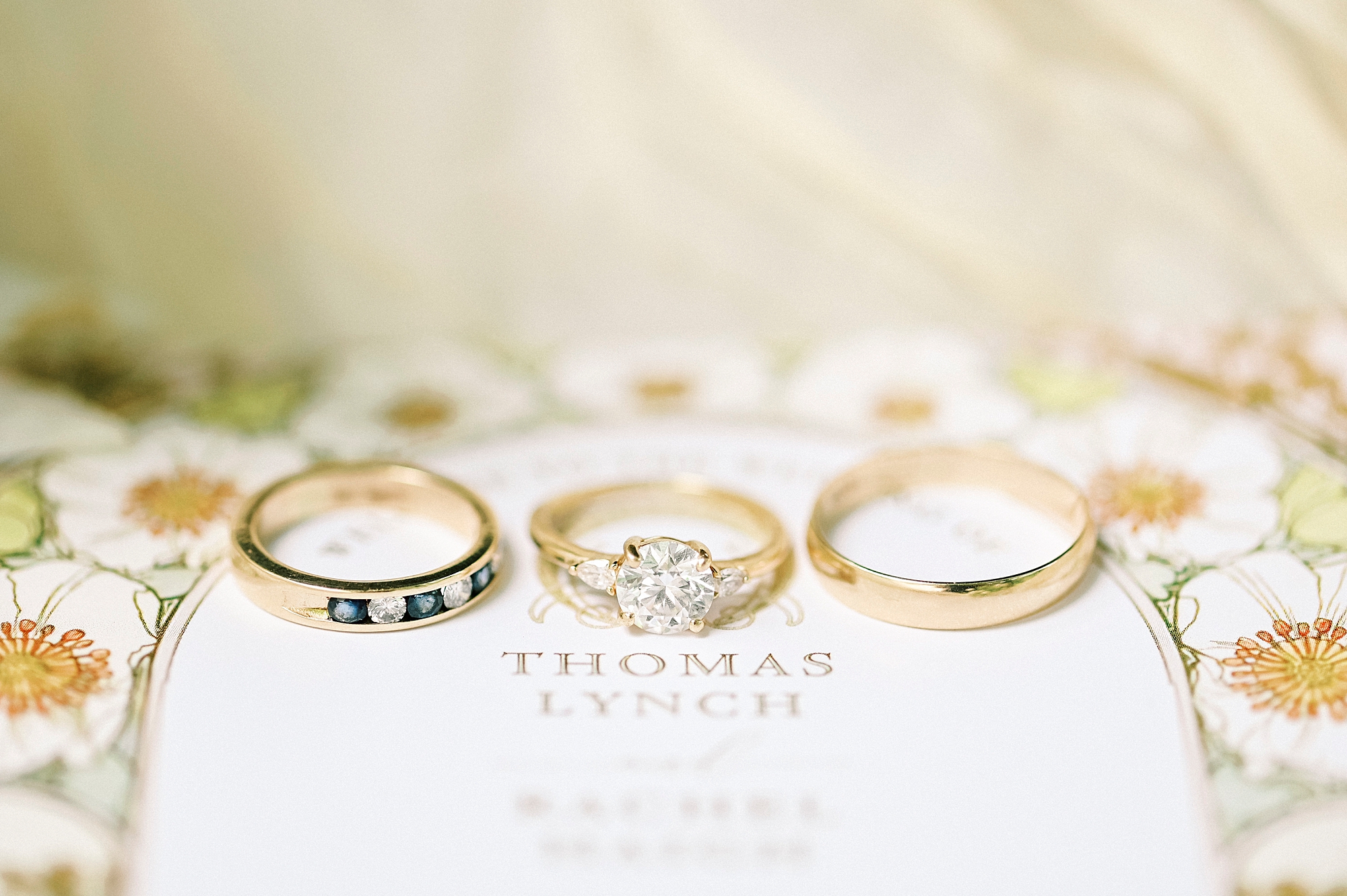 three gold bands laying on ivory invitation suite