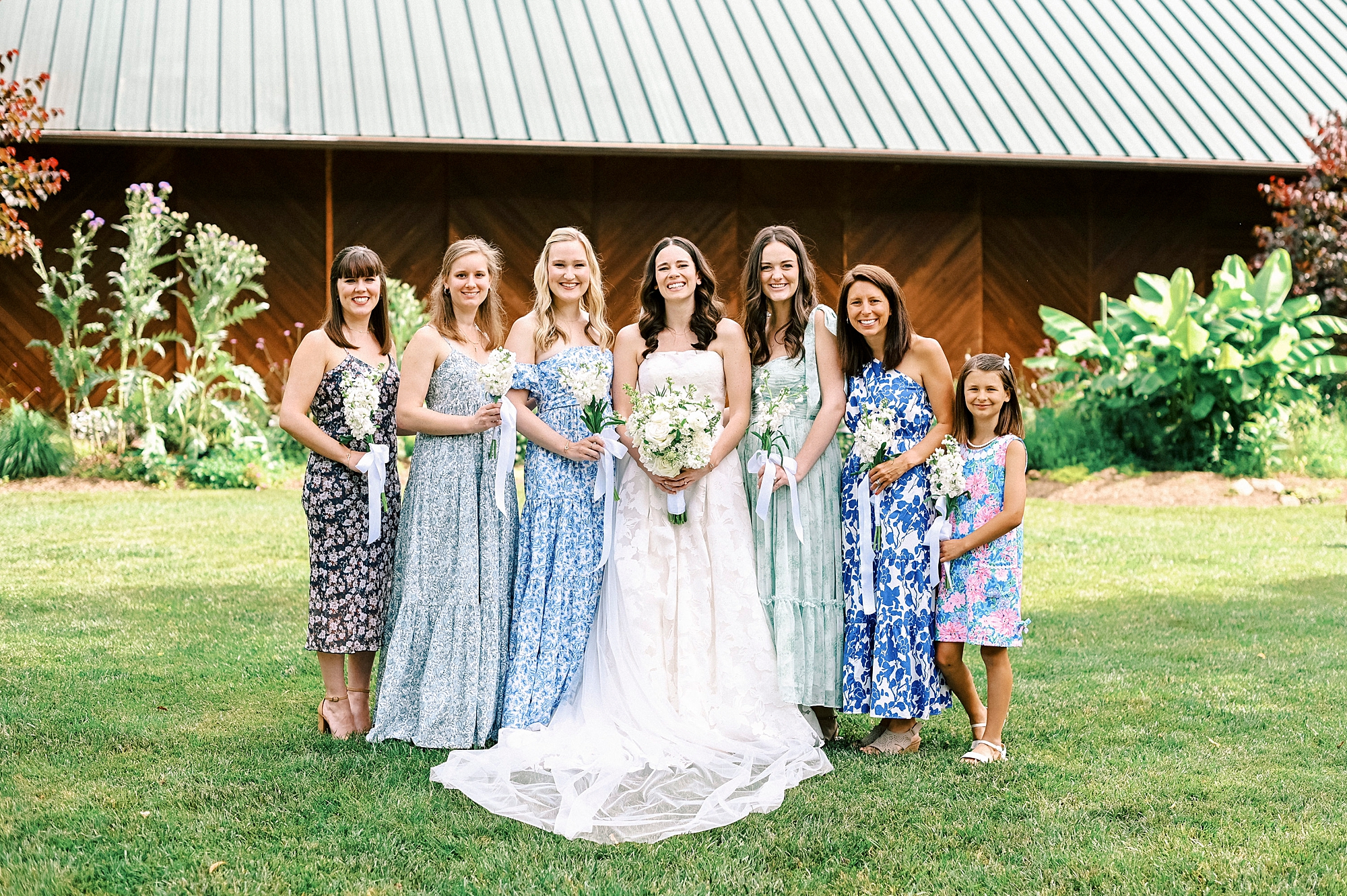 bride stands with bridesmaids in mismatched blue flower dresses